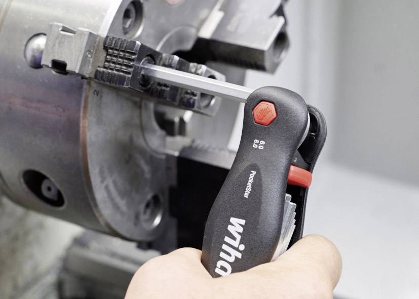 Stavební klíč se používá k utažení šroubu ve velké kovové strojní části. Ruka uživatele je viditelná.