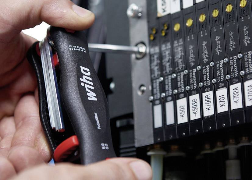 Osoba utahuje šroub na rozváděči pomocí šroubováku Wiha. Rozváděč obsahuje několik černých a bílých popisek.