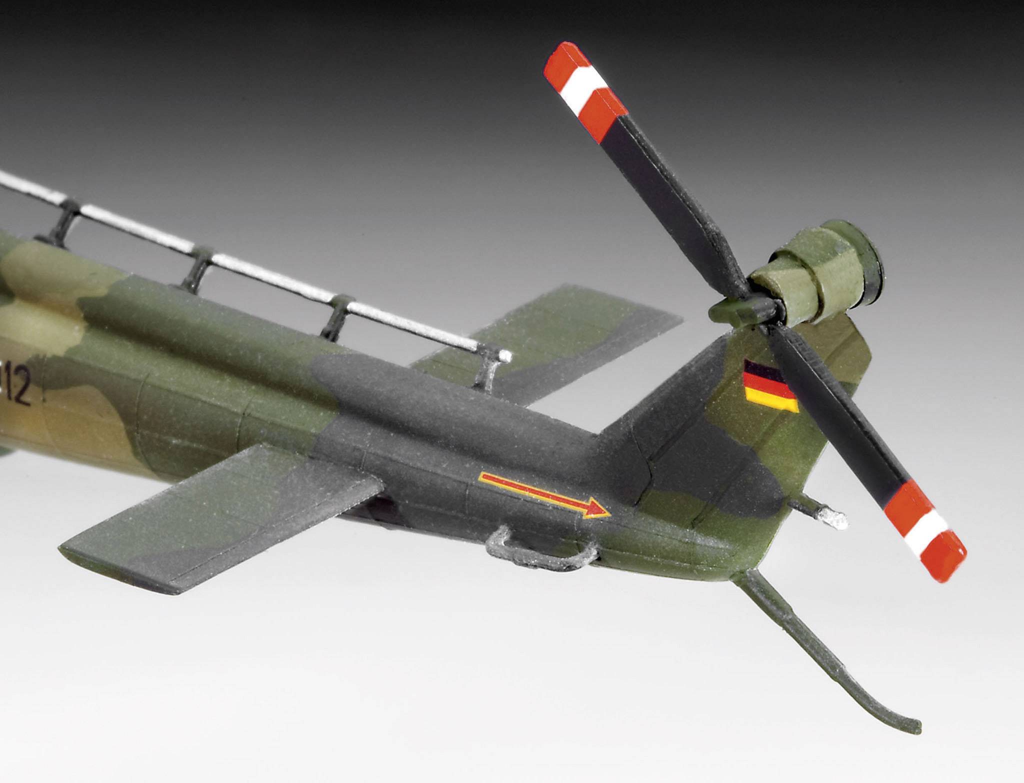 Model vojenské helikoptéry s maskováním a německým vlajkovým emblémem. Otočný zadní rotor s výraznými červenými pruhy.