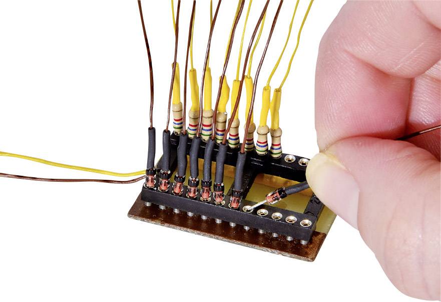 Jedna ruka pájedlem připájí dráty k černé elektronické desce s barevně kódovanými rezistory.
