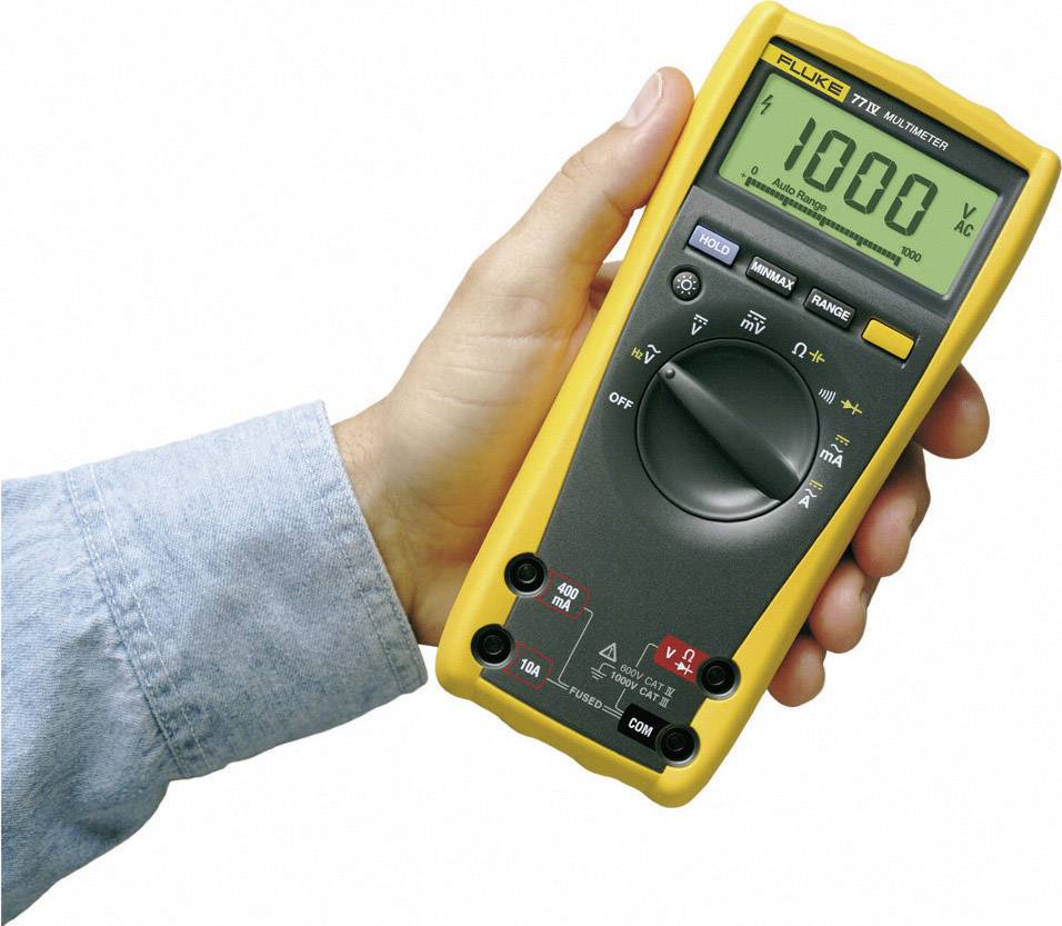 Jedna ruka drží digitální multimetr se žlutým pouzdrem. Display ukazuje '1000 V AC'.