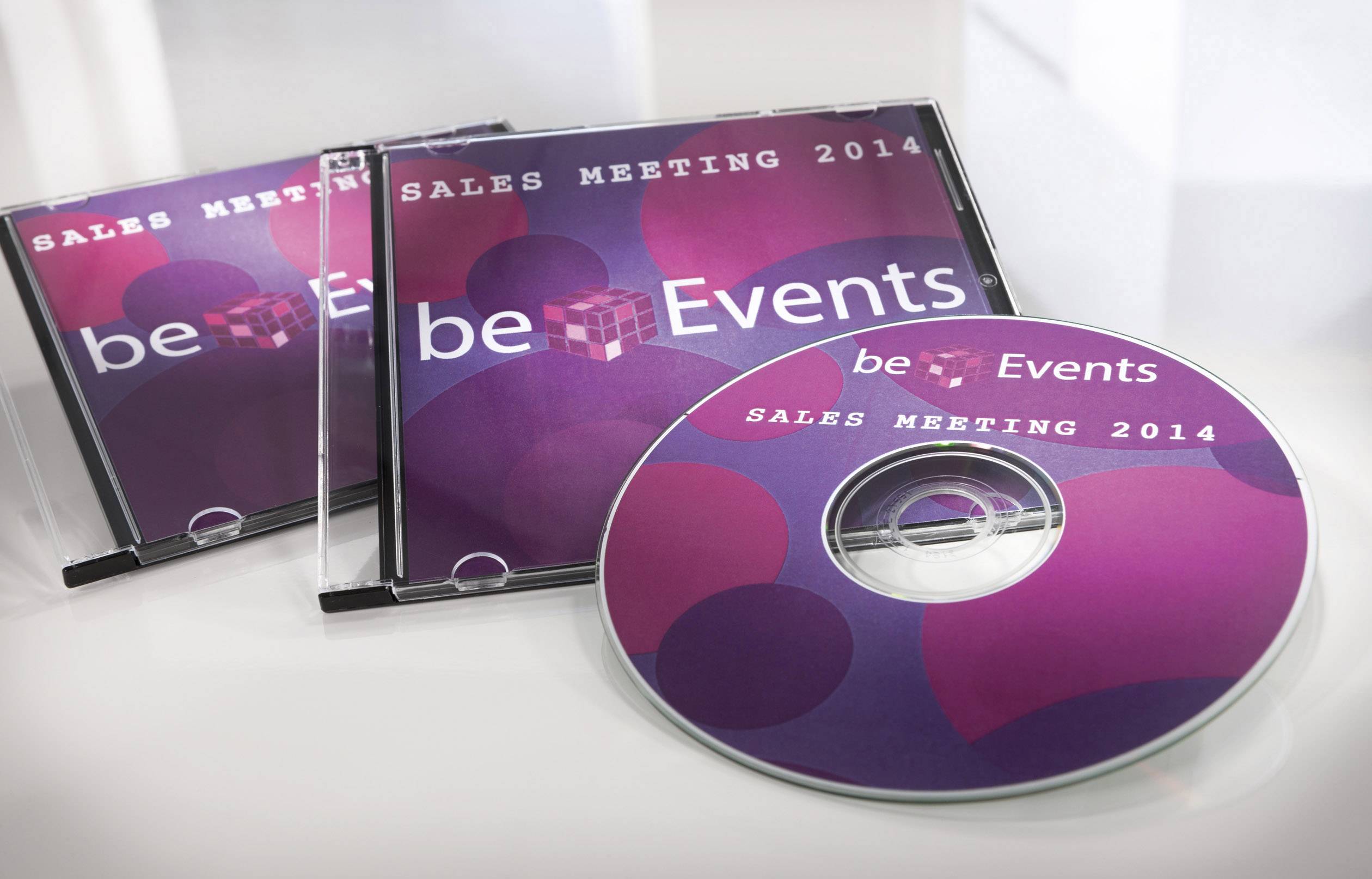 Několik obalů na CD a jeden CD disk s nápisem 'be Events Sales Meeting 2014' v odstínech fialové a růžové barvy.