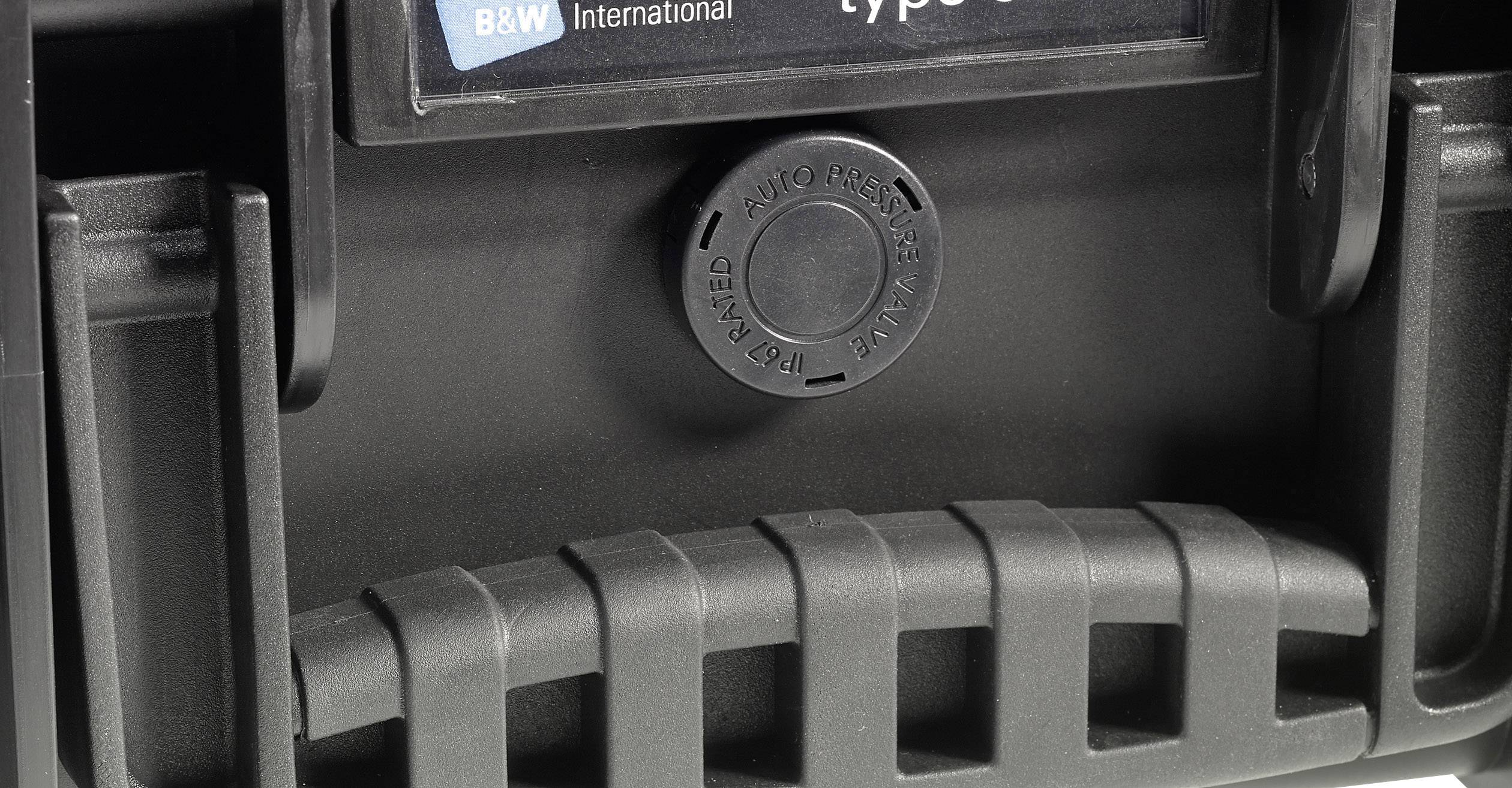Rukojeť pevného kufru s odvětrávacím ventilem uprostřed, který je označen nápisem 'AUTOMATICKÉ VYROVNÁNÍ TLAKU'.