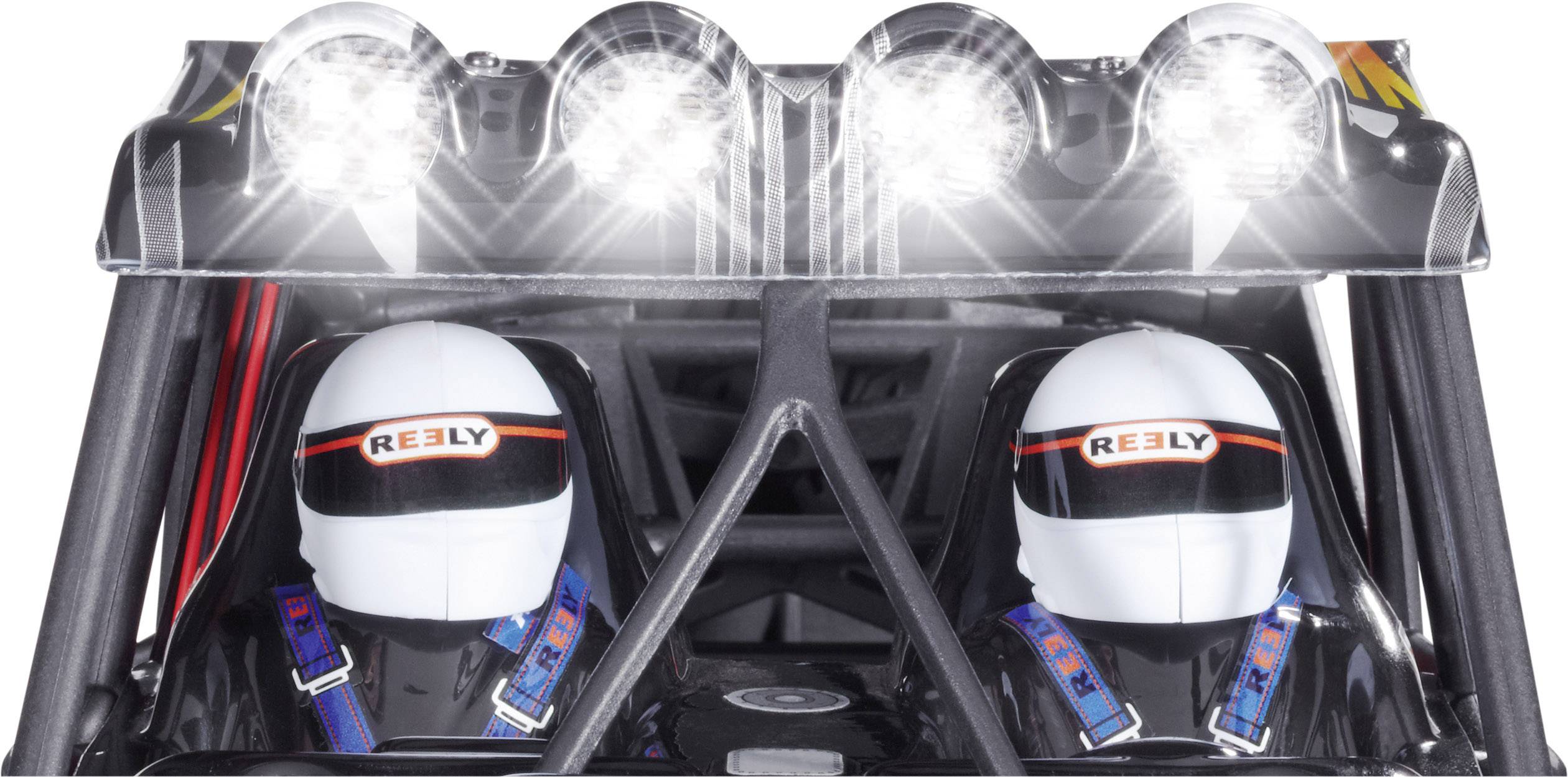 Dva závodníci s bílými helmami sedí vedle sebe ve vozidle. Nad nimi svítí jasná řada světlometů.