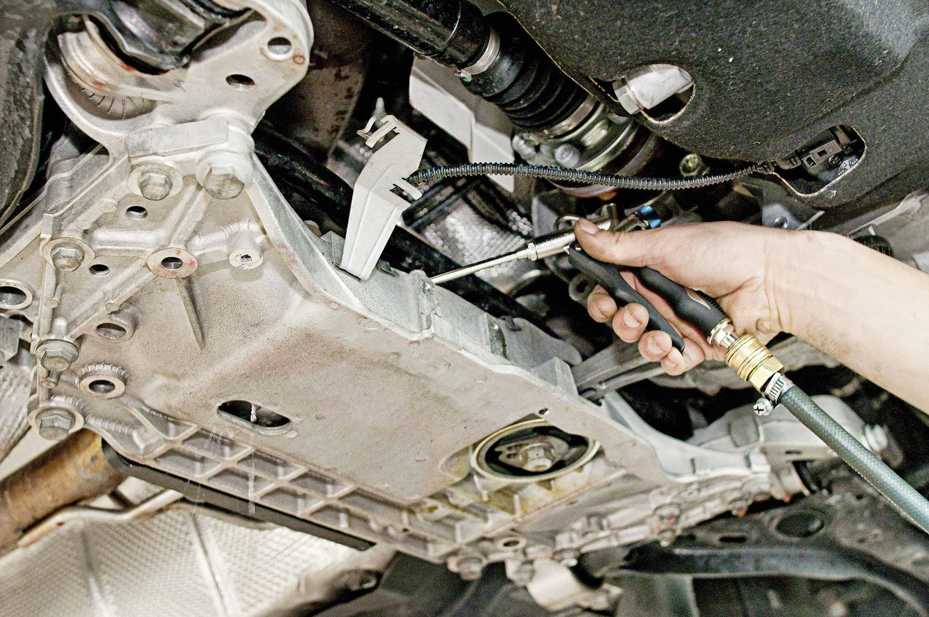 Osoba provádí opravu nebo údržbu automobilu. Nástroj je přiložen k součásti z kovu.