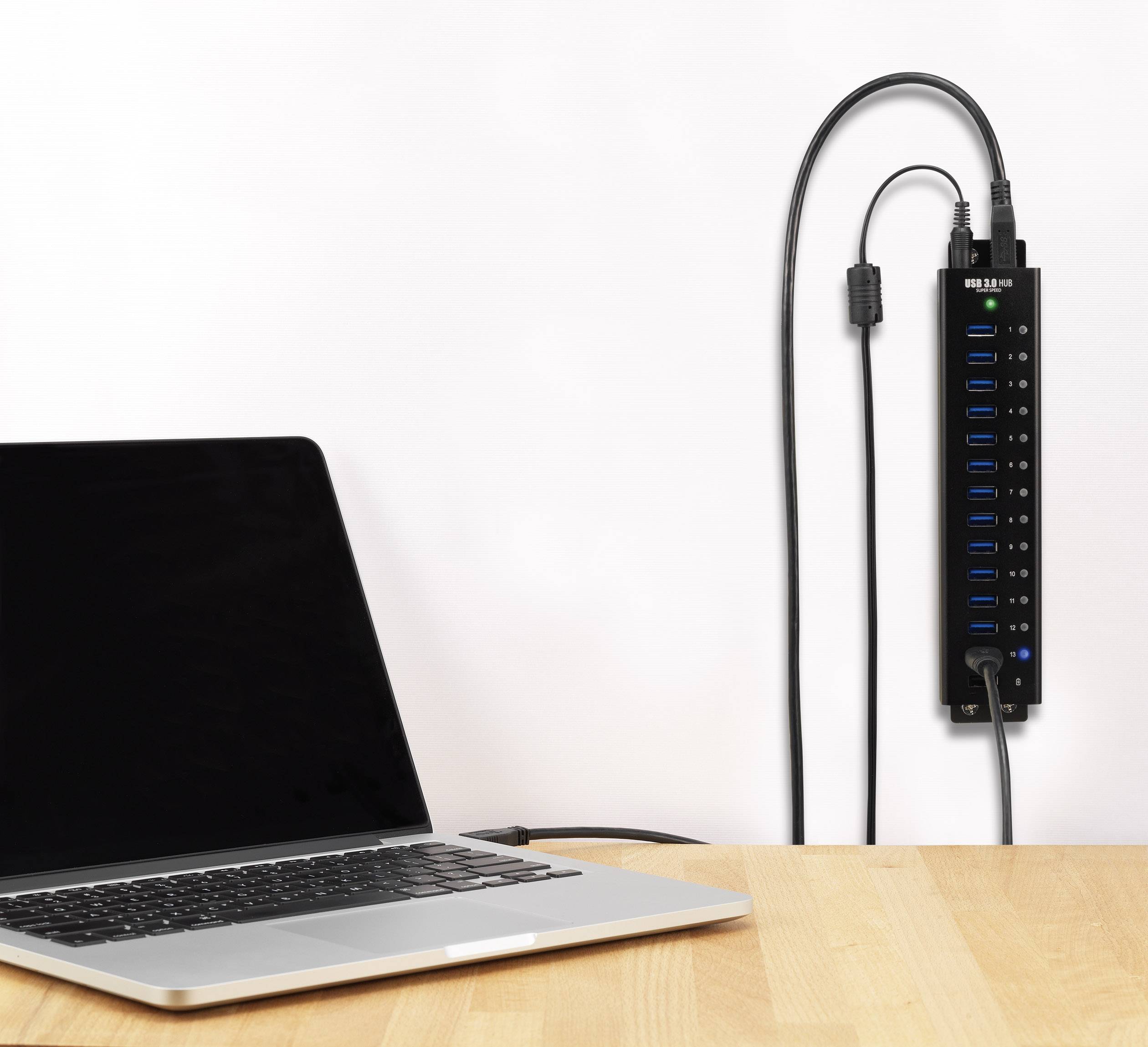 Laptop je připojen k USB rozbočovači namontovanému na stěně; je vidět několik USB portů a kabelů.