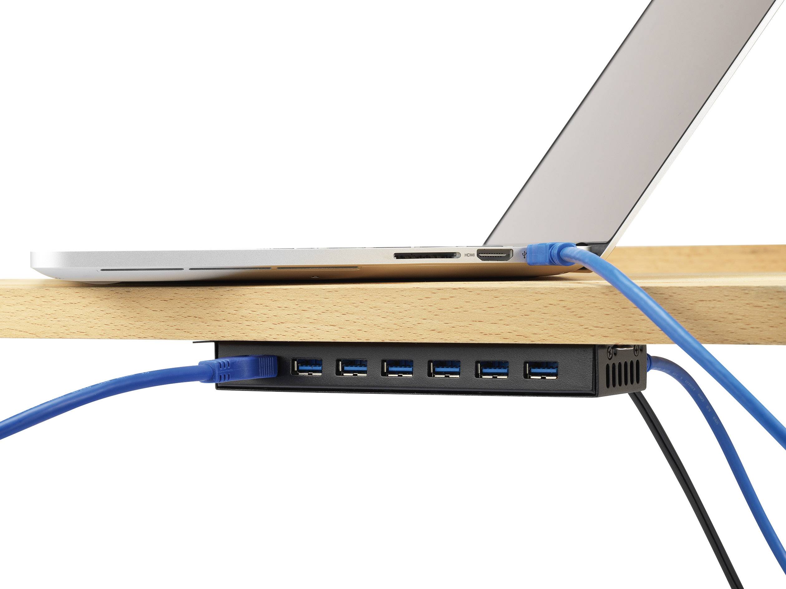 Laptop je připojen modrými USB kabely k USB rozbočovači, který je připevněn pod dřevěným povrchem. Rozbočovač má několik portů.