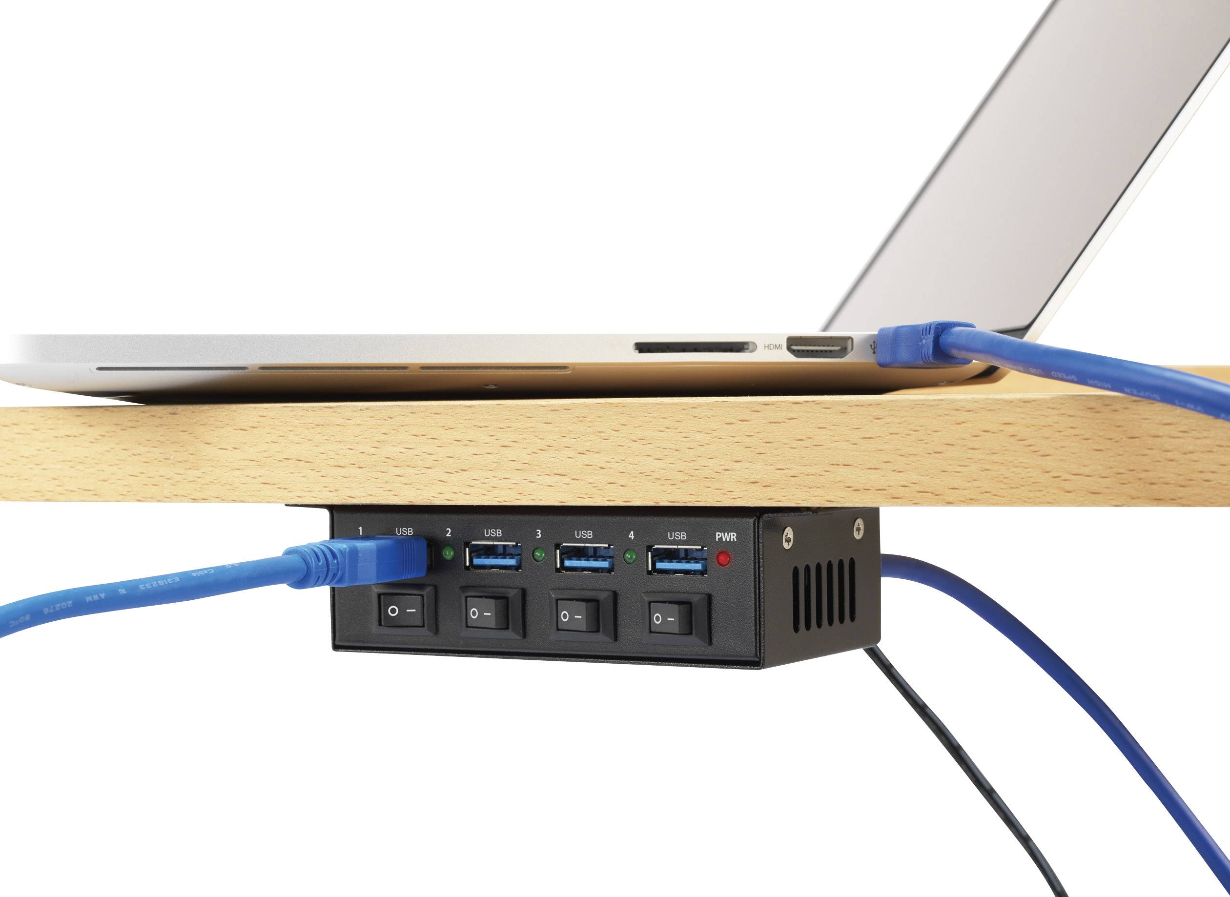Laptop je připojen k USB rozbočovači namontovanému pod stolem, který obsahuje několik modrých a černých kabelů pro přenos dat a napájení.
