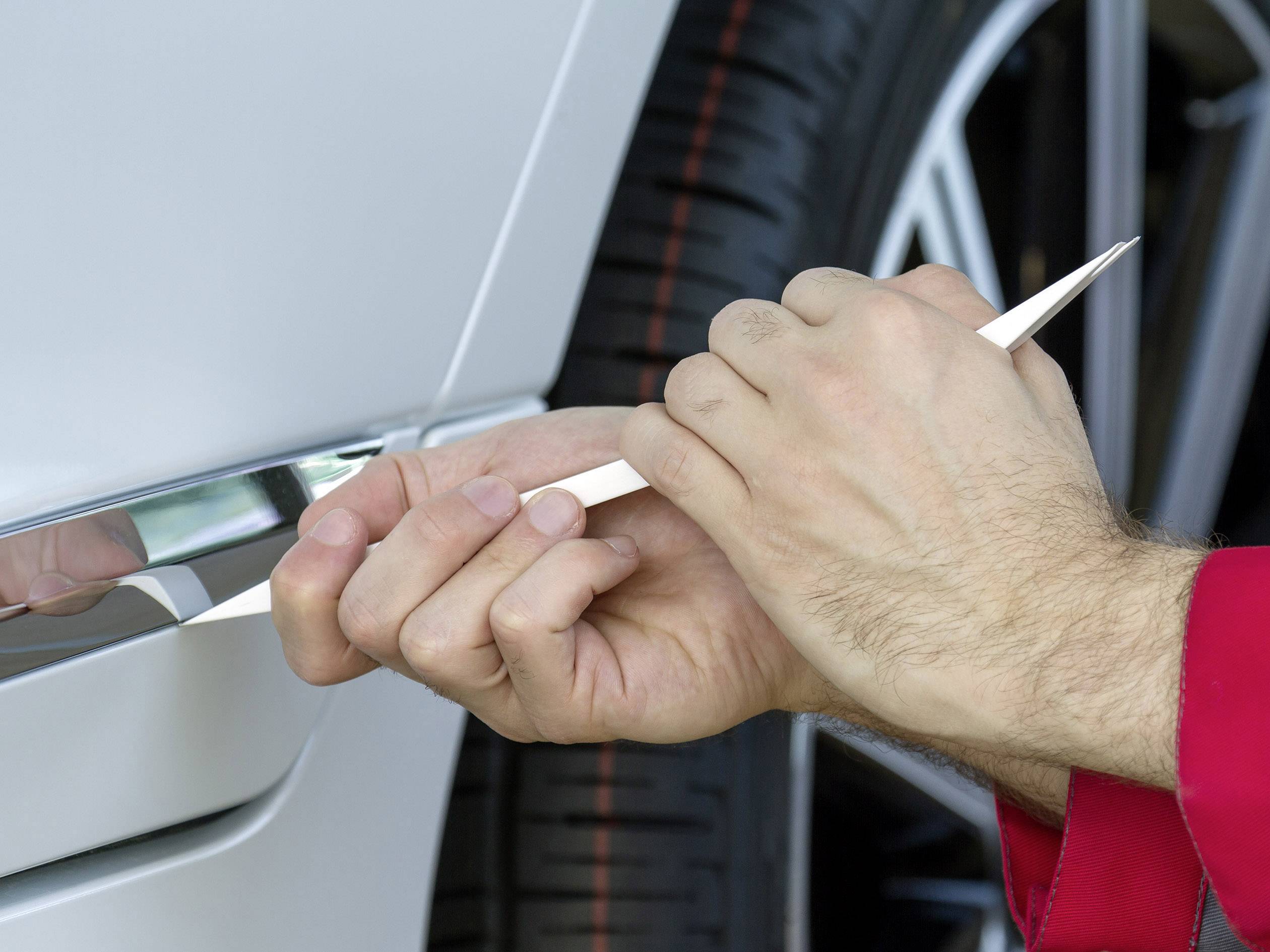 Precizní práce na bílém automobilu. Jedna osoba používá plastový nástroj k opracování části karoserie nebo ozdobné lišty.