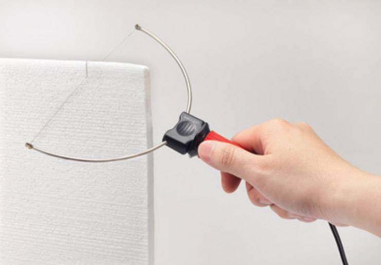 Ruka držící elektrický řezací nástroj s horním drátem řeže do bílého kousku pěnové hmoty.