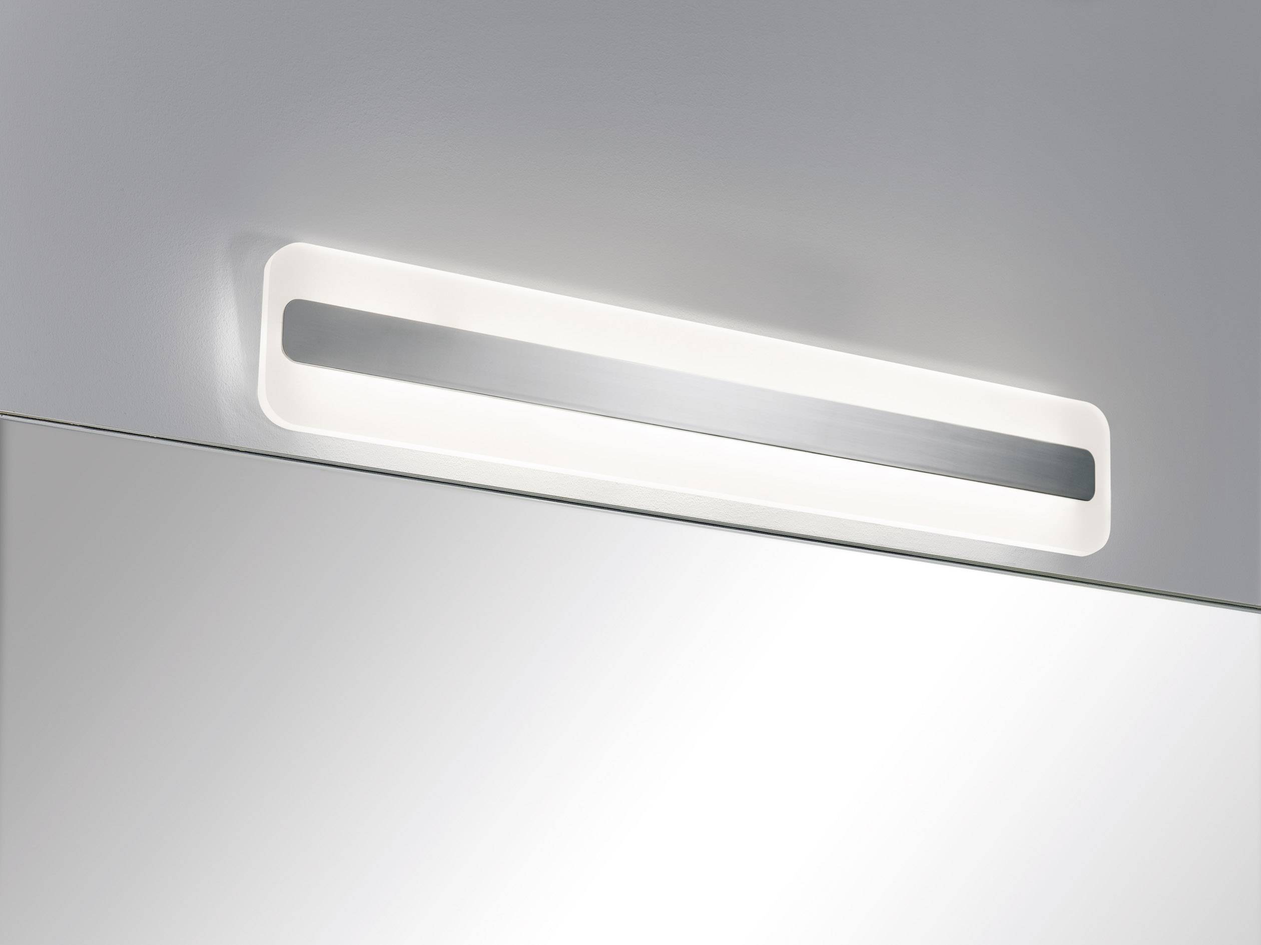 Podlouhlá moderní lampa s jasně bílým světlem, namontovaná nad zrcadlem na stěně, je vhodná pro rovnoměrné osvětlení.