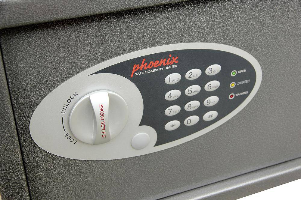 Elektronický trezor se zámkem na číselný kód. Je vidět značka 'Phoenix'. Tlačítka pro zadávání číselné kombinace a otočný knoflík pro odemčení.