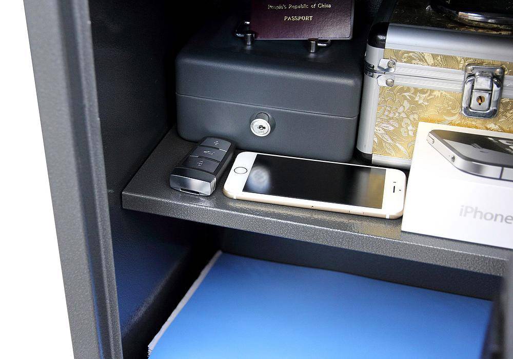 Vnitřní pohled do trezoru s mobilním telefonem, klíčem od auta, cestovním pasem a malou uzavřenou kovovou schránkou na polici.