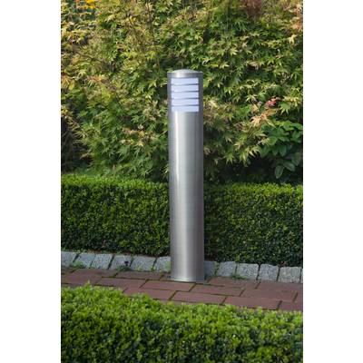 Moderní zahradní lampa z kovu stojí v udržované zahradě s rostlinami a keři v pozadí.