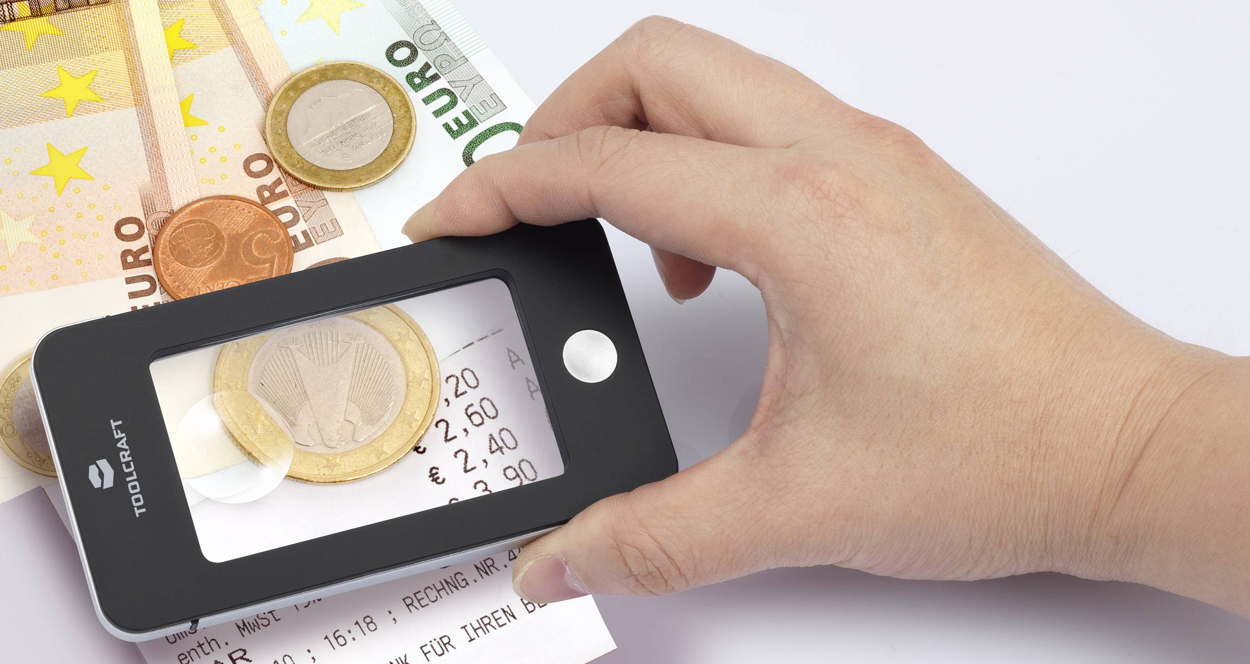 Ruka drží lupu nad bankovkami, mincemi a účtenkou. Viditelné částky jsou 2,20 EUR, 2,40 EUR a 7,90 EUR.