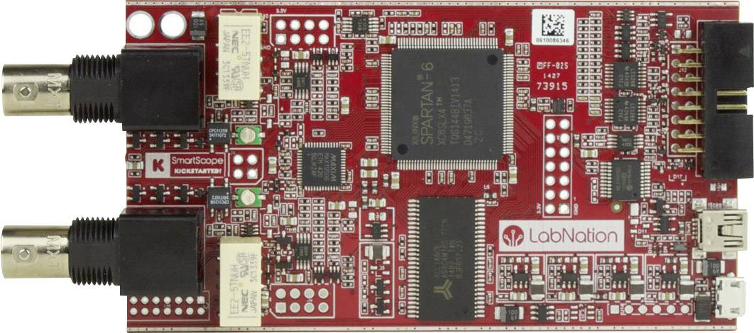 Červená deska plošných spojů s různými elektronickými komponenty, dvěma černými konektory a velkým mikročipem uprostřed.