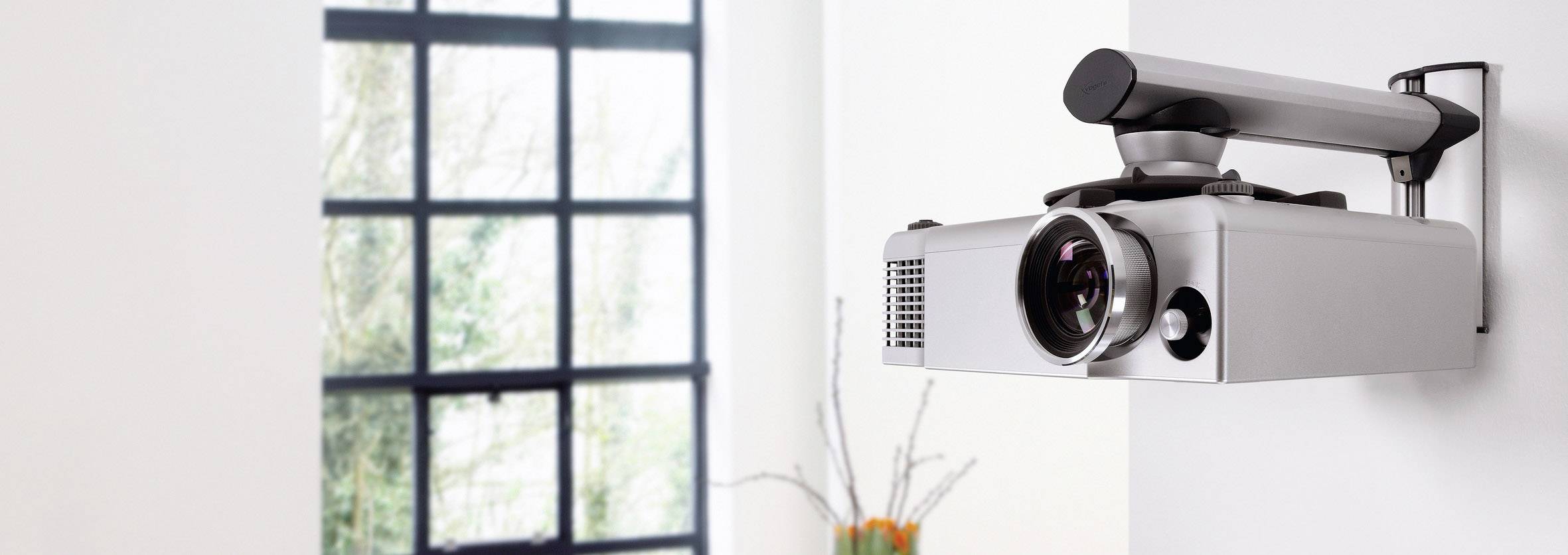 Moderní projektor je připevněn na stěně před velkým oknem. V pozadí stojí minimalistické vázy.