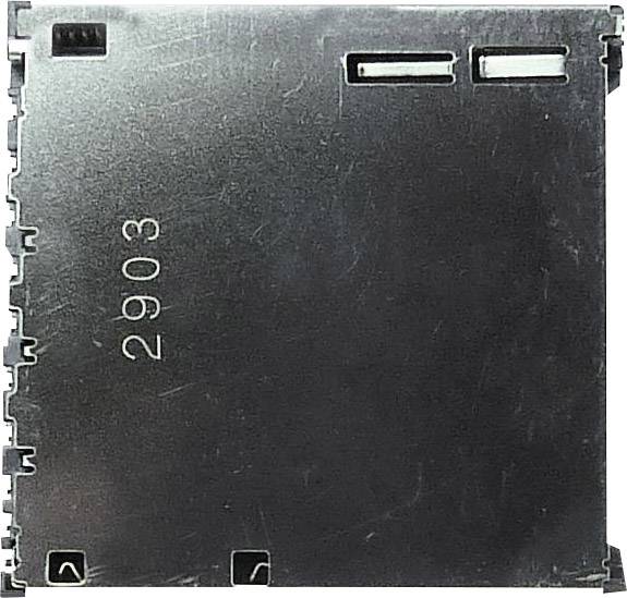 Abstraktní čtvercový kovový díl s vtisknutým číslem '2903'. Vlevo a nahoře jsou viditelné malé elektrické konektory.