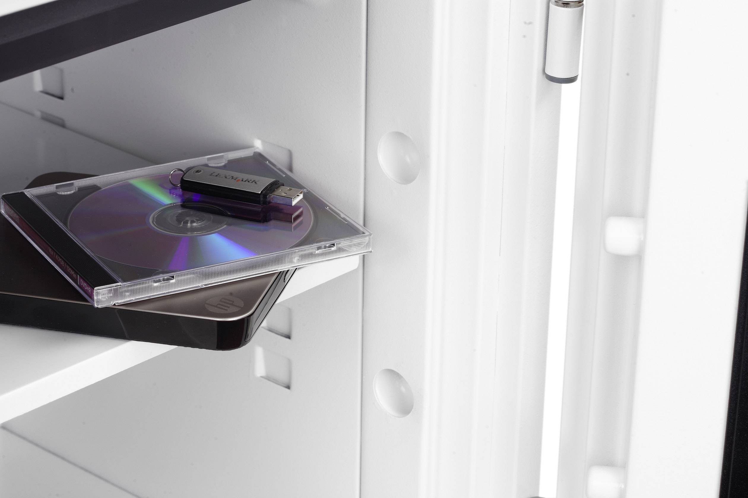 Otevřený trezor ukazuje USB disk a CD na polici. Důraz je kladen na bezpečné uchovávání digitálních médií.