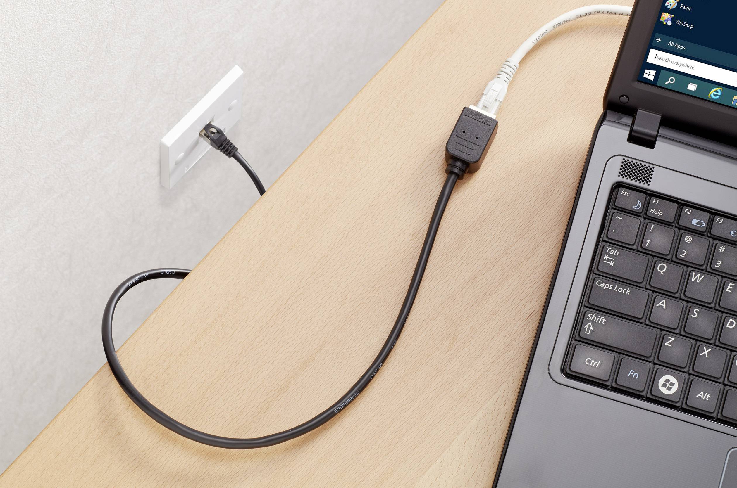 Notebook je připojen ethernetovým kabelem do nástěnné zásuvky. Na obrazovce je zobrazeno okno operačního systému.