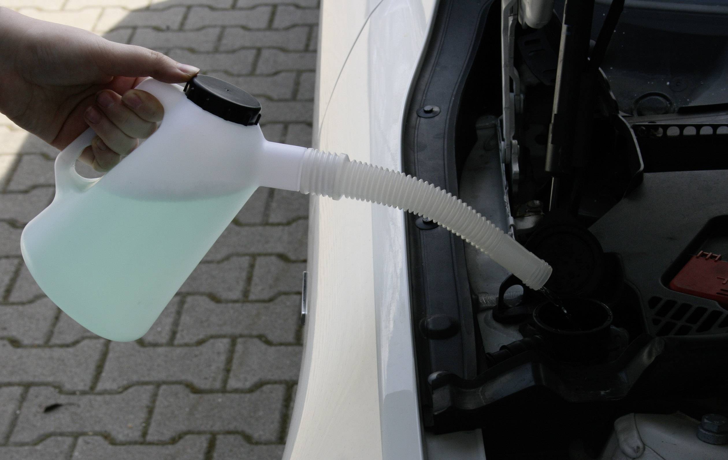 Ruka plní nádobku ostřikovačů modrou kapalinou z lahve v automobilu.