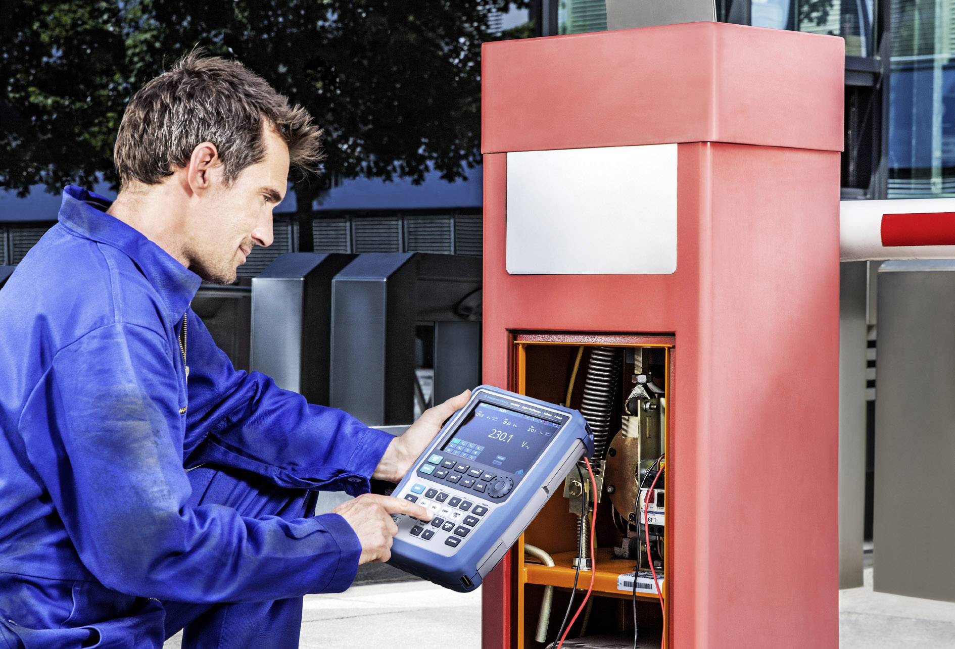 Technik v modré pracovní kombinéze kontroluje parkovací automat elektronickým zařízením na uzavřeném parkovišti.