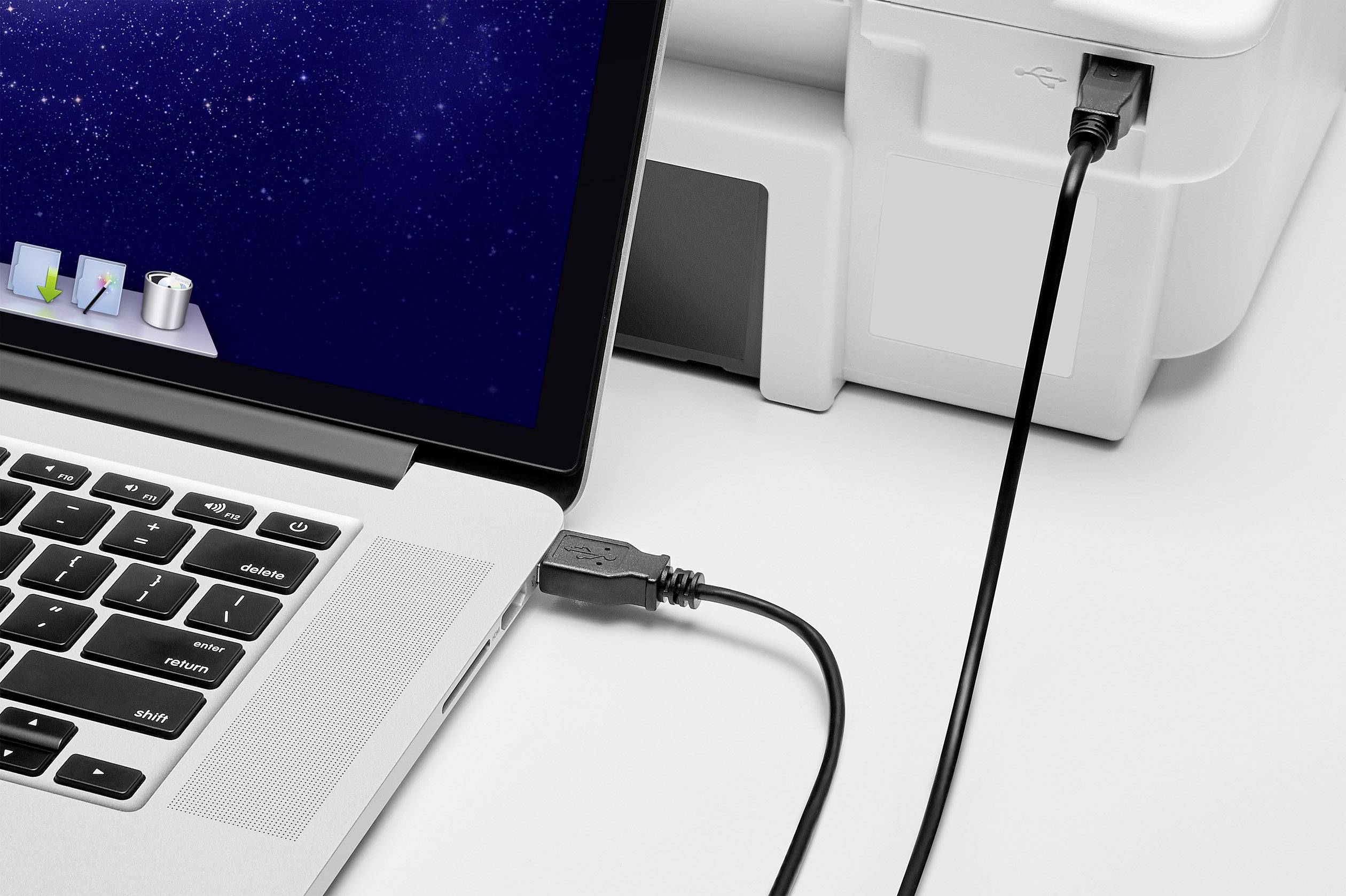 Laptop je připojen k tiskárně pomocí USB kabelu, což naznačuje probíhající tisk nebo přenos dat.