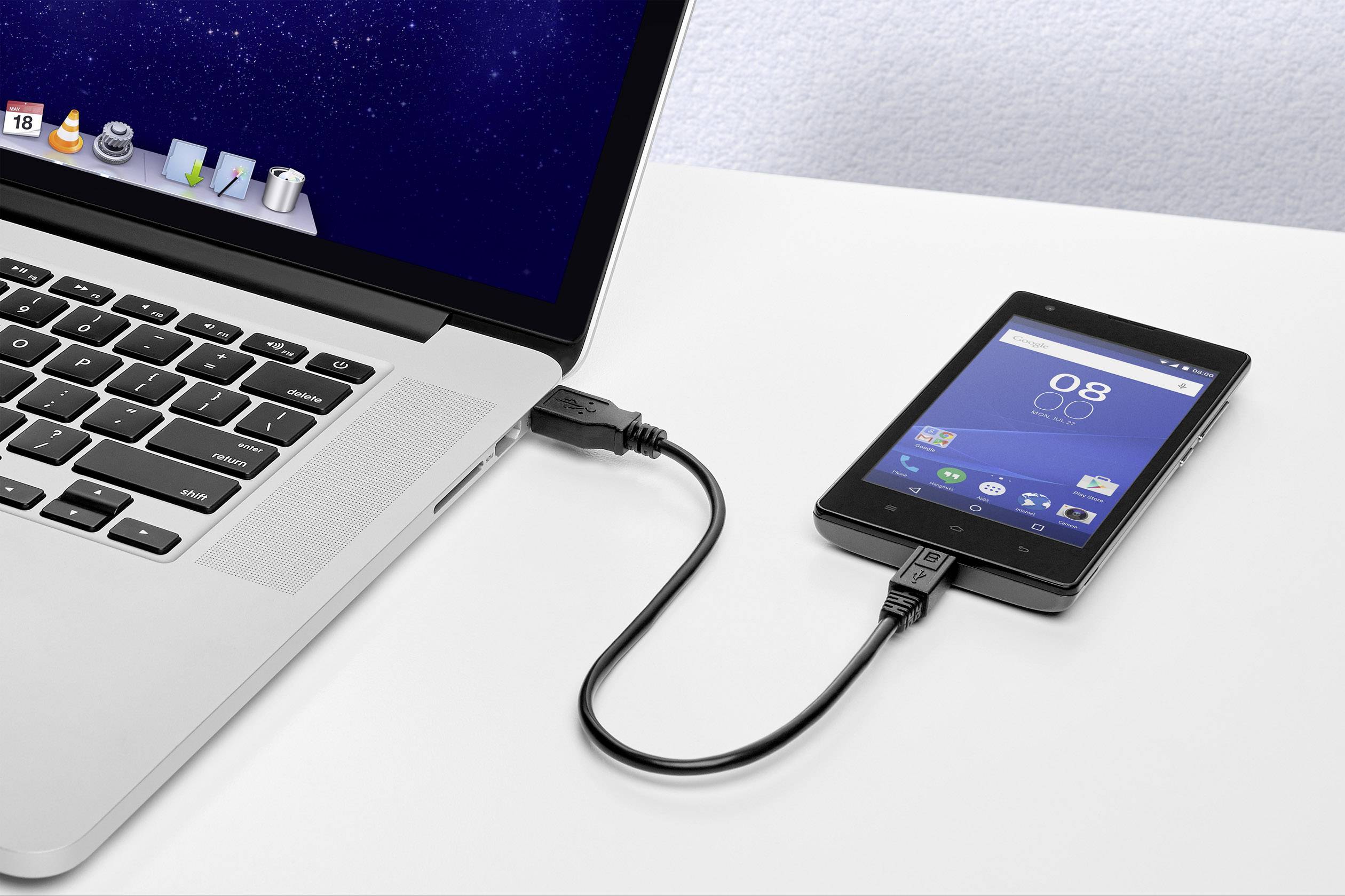 Přenosný počítač je připojen k mobilnímu telefonu pomocí USB kabelu. Obě zařízení jsou zapnutá; zdá se, že probíhá výměna dat.