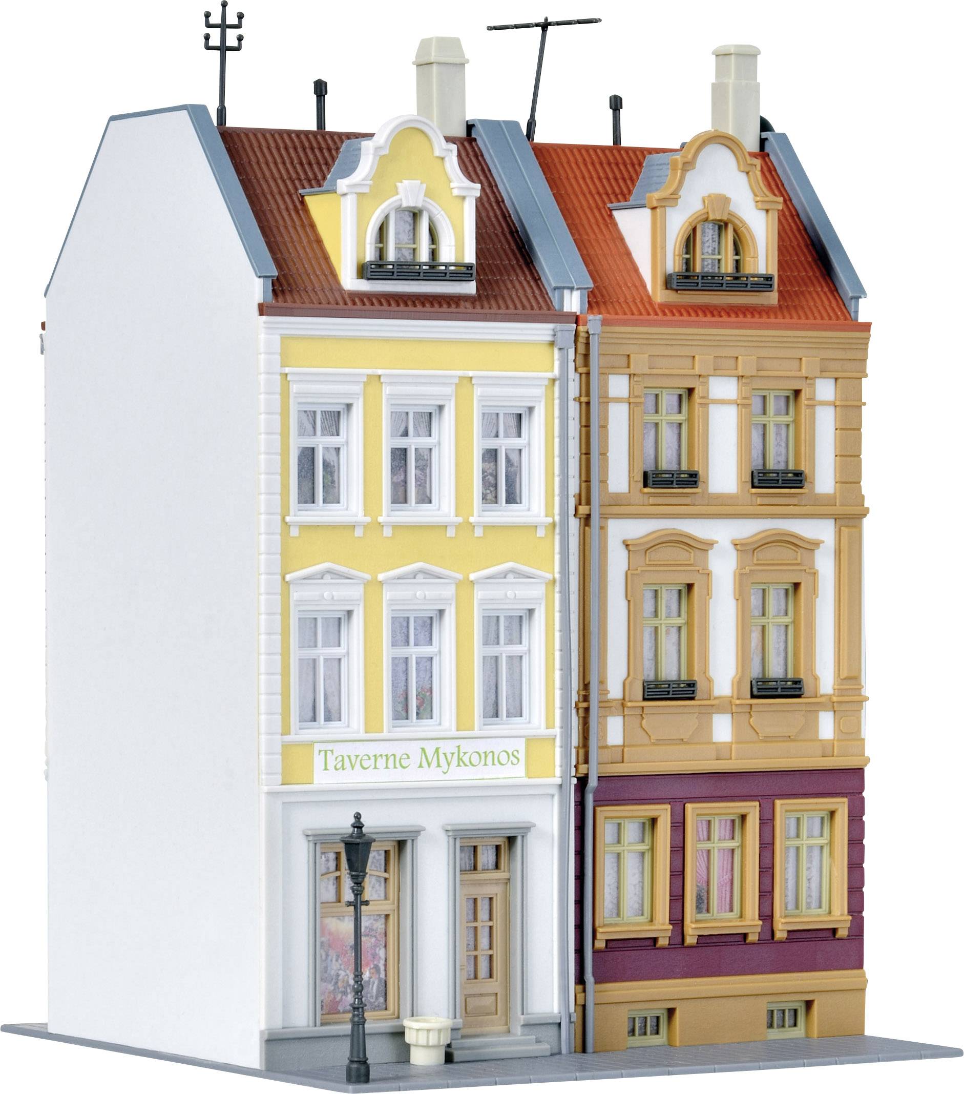 Dva vedle sebe stojící modelové domy s ozdobenými fasádami. Jeden má žlutý, druhý pískový vnější plášť. Mezi nimi stojí cedule s nápisem 'Taverna Mykonos'.