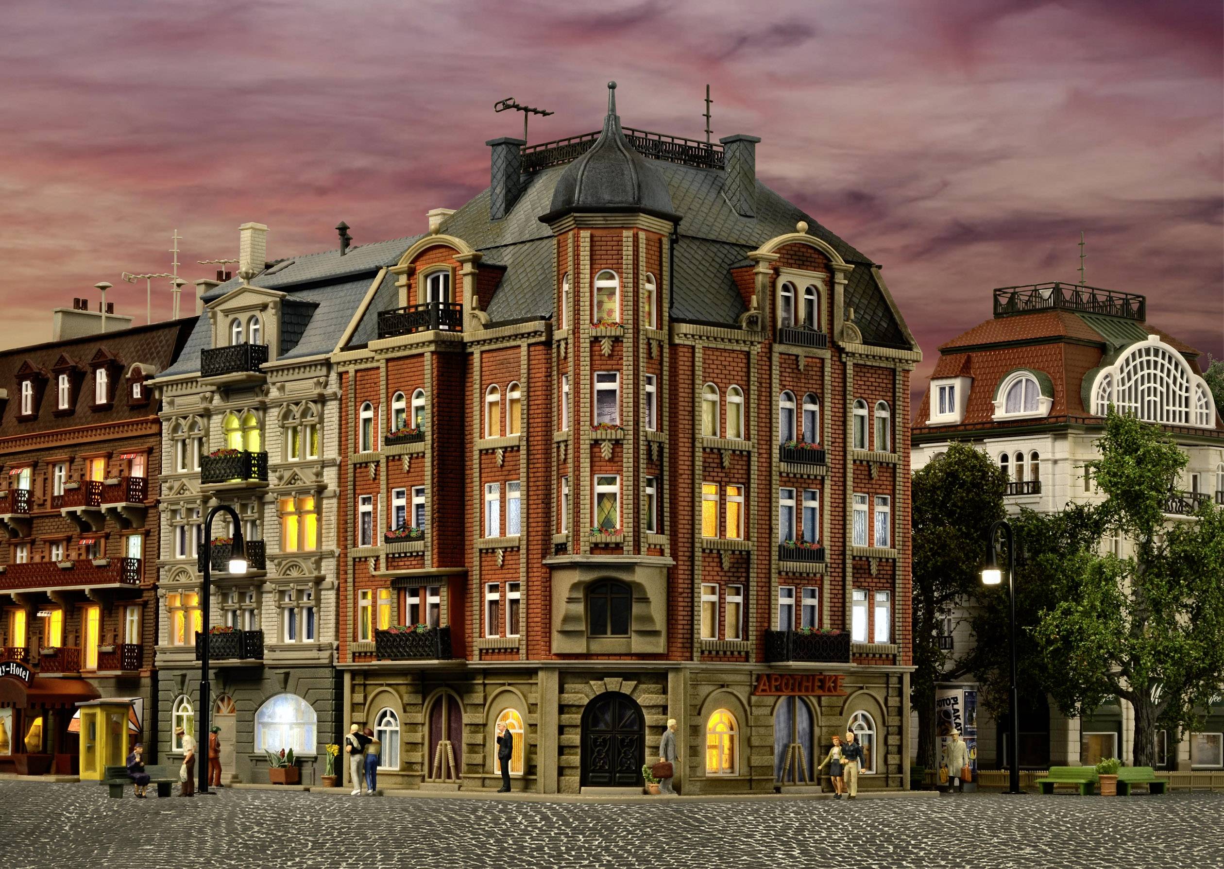 Osvětlená historická budova se složitou architekturou a detaily, obklopená okolními domy při západu slunce.