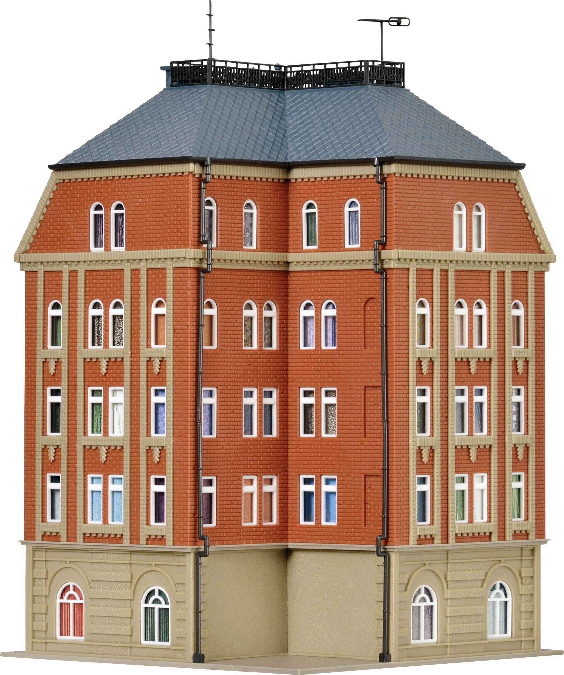 Velká, vícepodlažní budova s červenou cihlovou fasádou a tmavě šedou střechou. Mnoho oken, architektonické ozdoby.