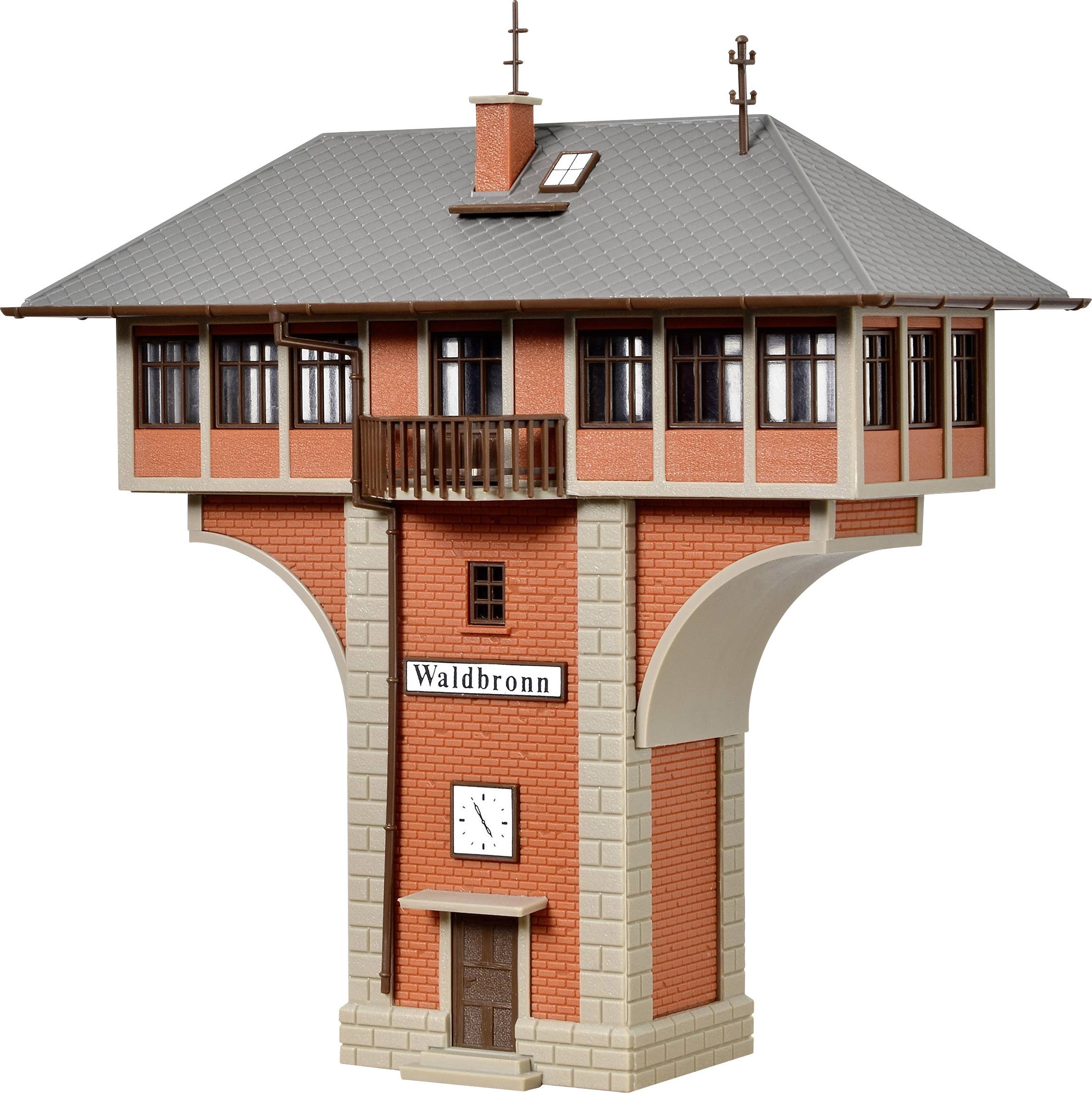 Malý model výpravní budovy s nápisem 'Waldbronn'. Budova má červené cihlové zdi, okna a hodiny na přední straně.