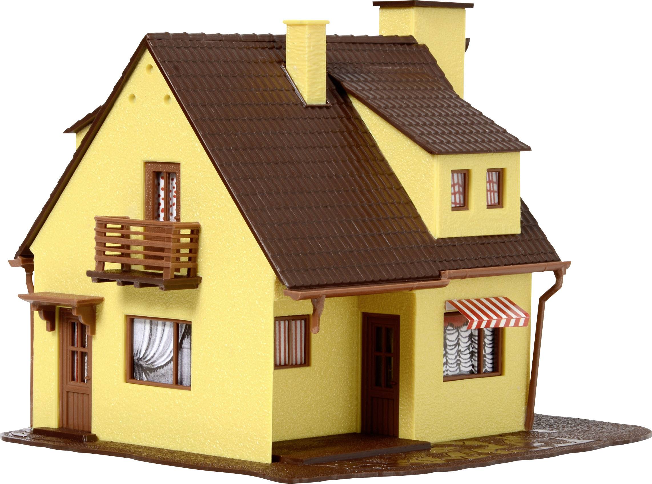 Malý žlutý modelový dům s hnědou střechou, balkónem a komínem. Dům má dvě dveře a okenice s pruhovanou stříškou.