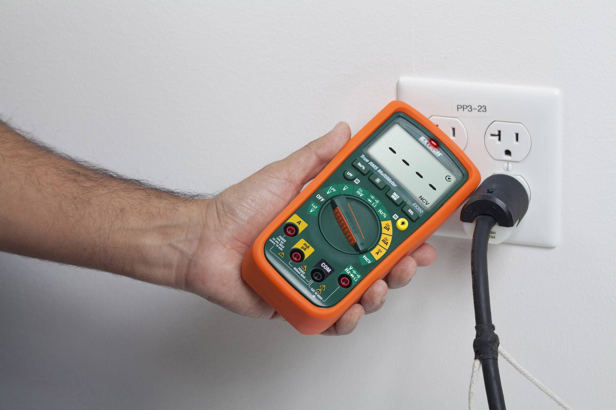 Jedna ruka drží multimetr, který je připojen do elektrické zásuvky za účelem provedení elektrických měření.