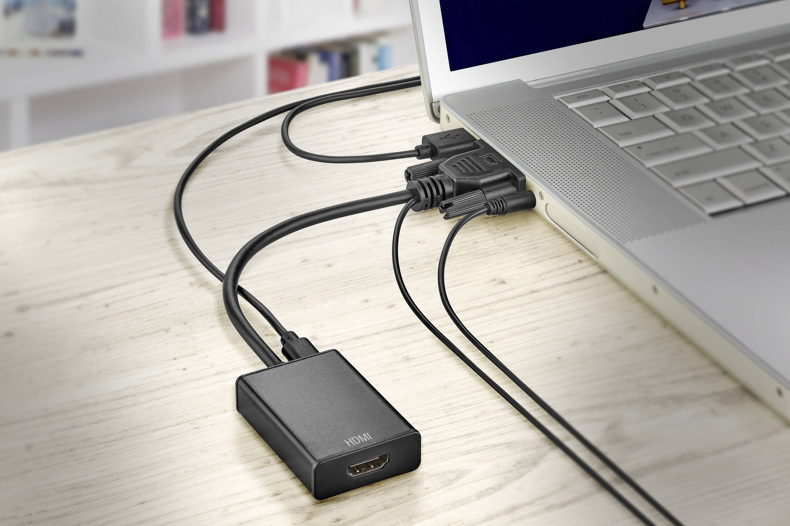 Notebook je připojen několika kabely k HDMI adaptéru, který leží na dřevěném stole.