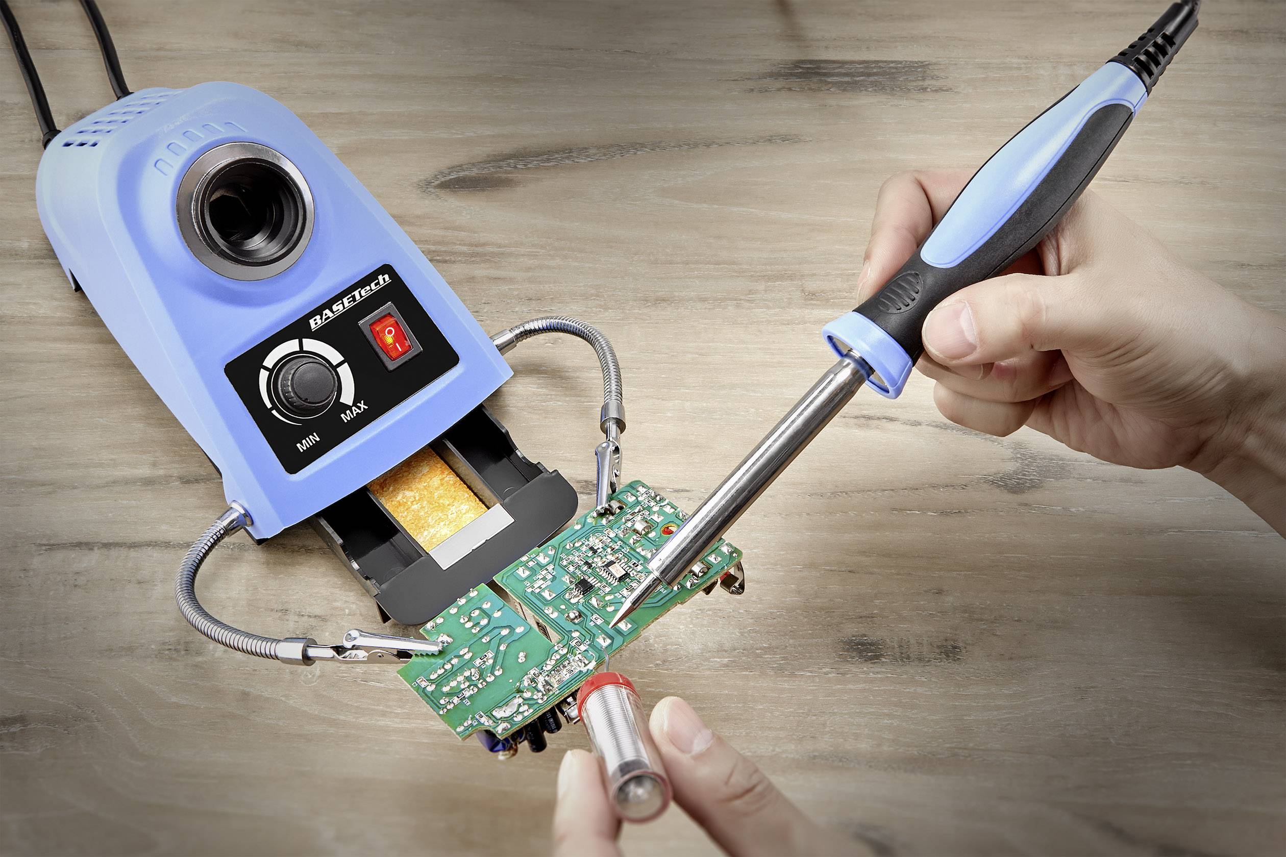 Pájecí pero se používá k pájení elektronického obvodu na zelené desce plošných spojů; v pozadí je jasně osvětlená pájecí stanice.