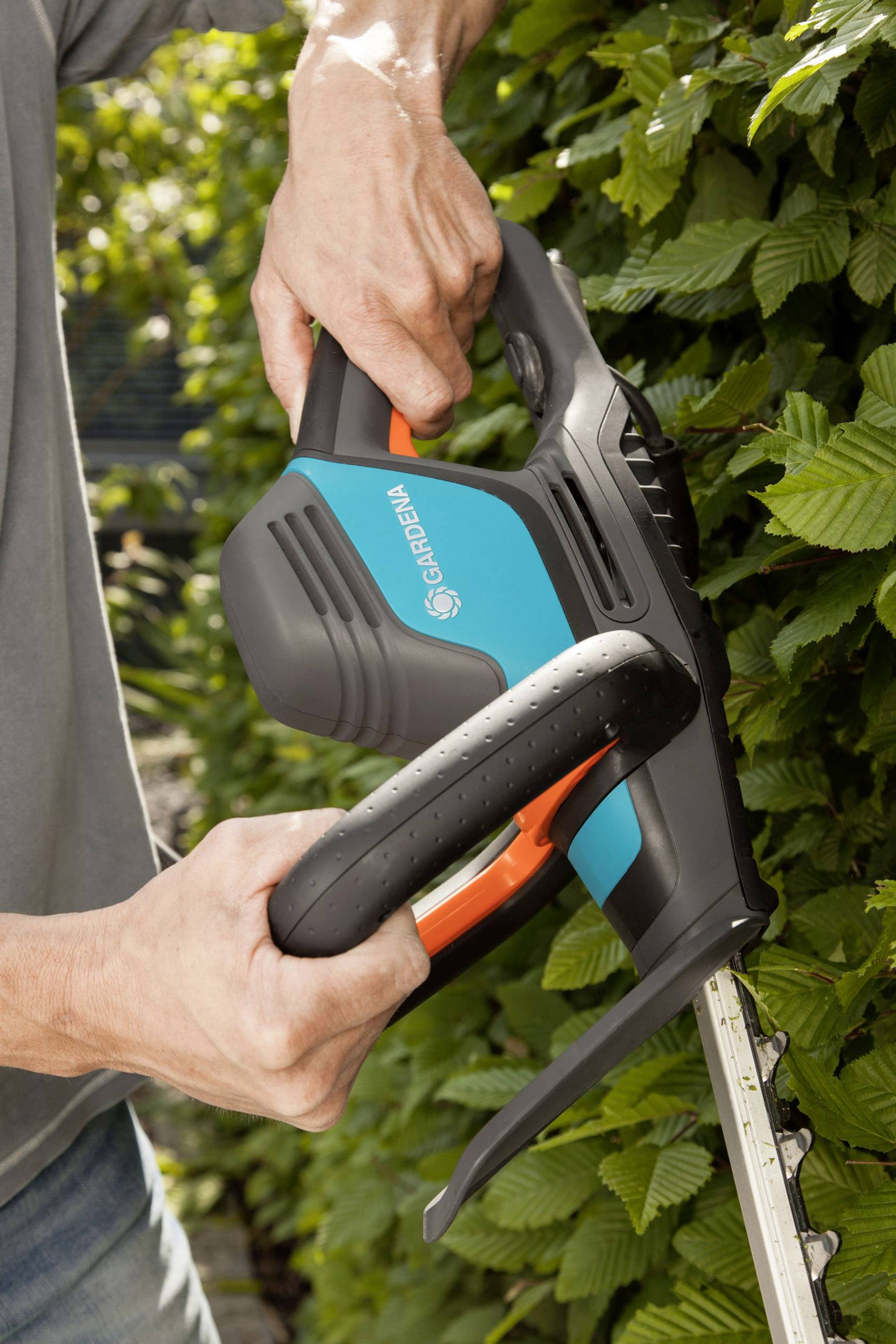 Muž stříhá křoví elektrickými nůžkami značky Gardena.