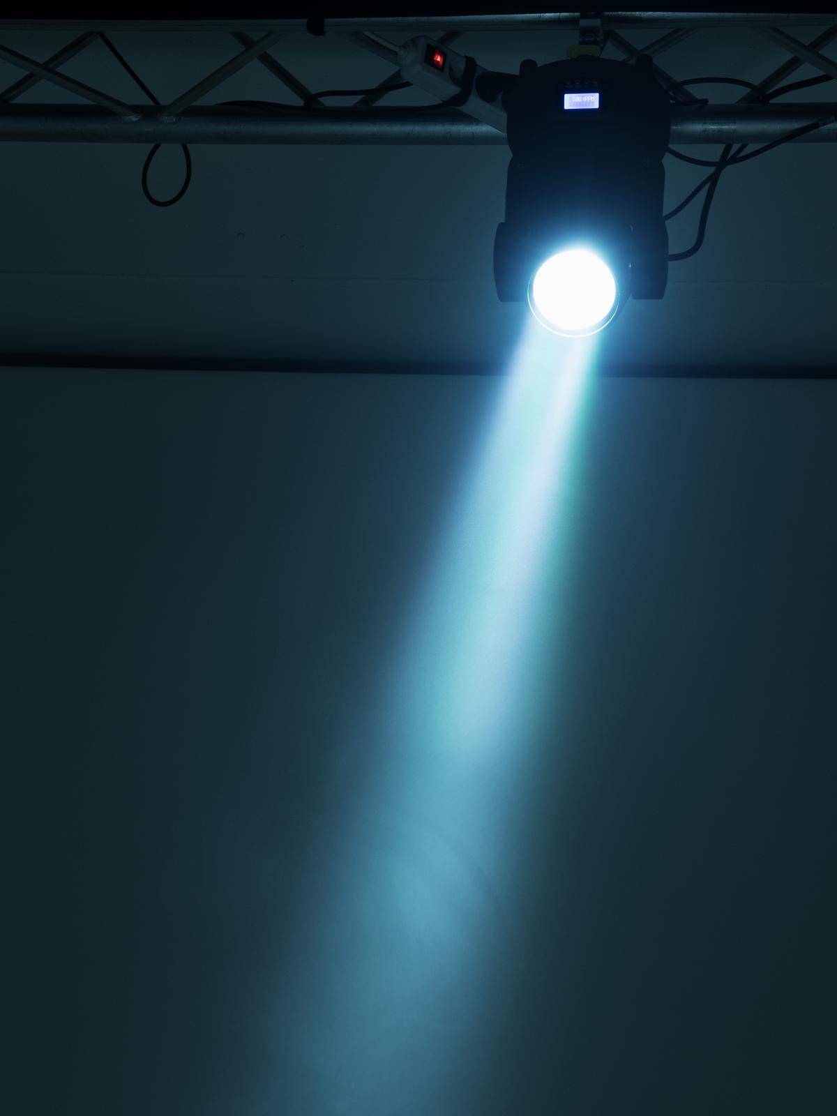 Jasný reflektor svítí shora na neutrální, prázdnou plochu a vytváří soustředěný světelný kužel před tmavým pozadím.
