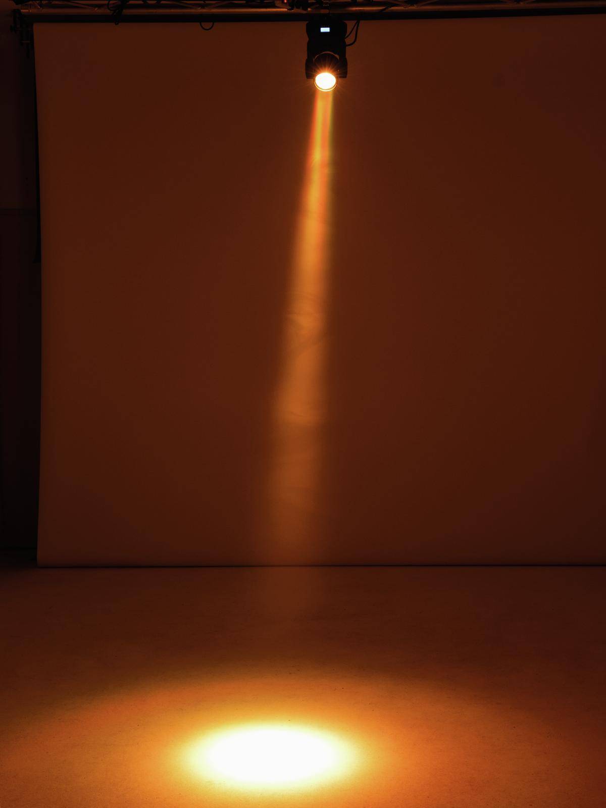 Jeden osamocený reflektor vrhá světelný kužel na podlahu, obklopený tmou.