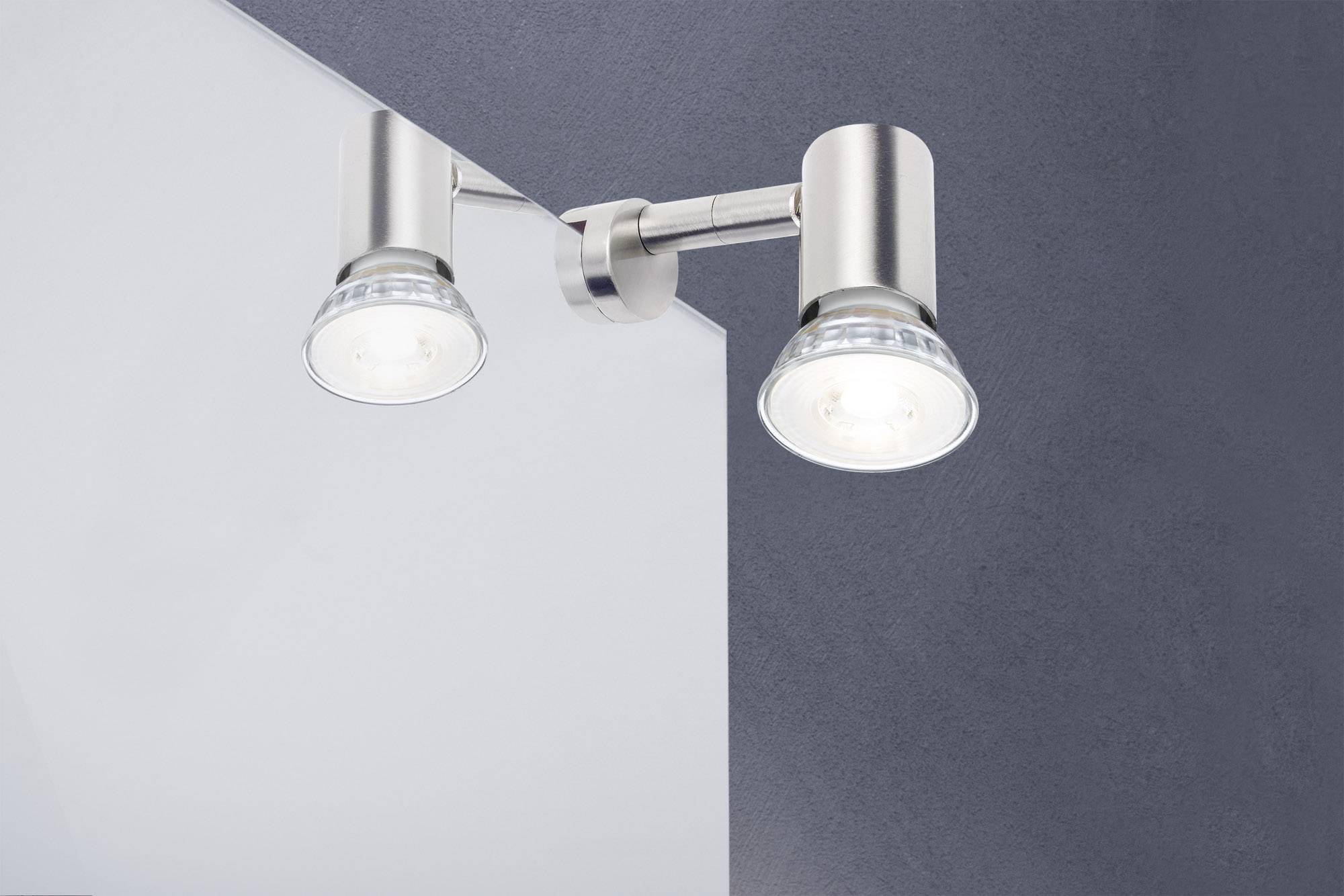 Dvě moderní, pochromované nástěnné lampy s průhlednými skleněnými stínidly jsou připevněny na stěně a svítí dolů. Minimalistický design.