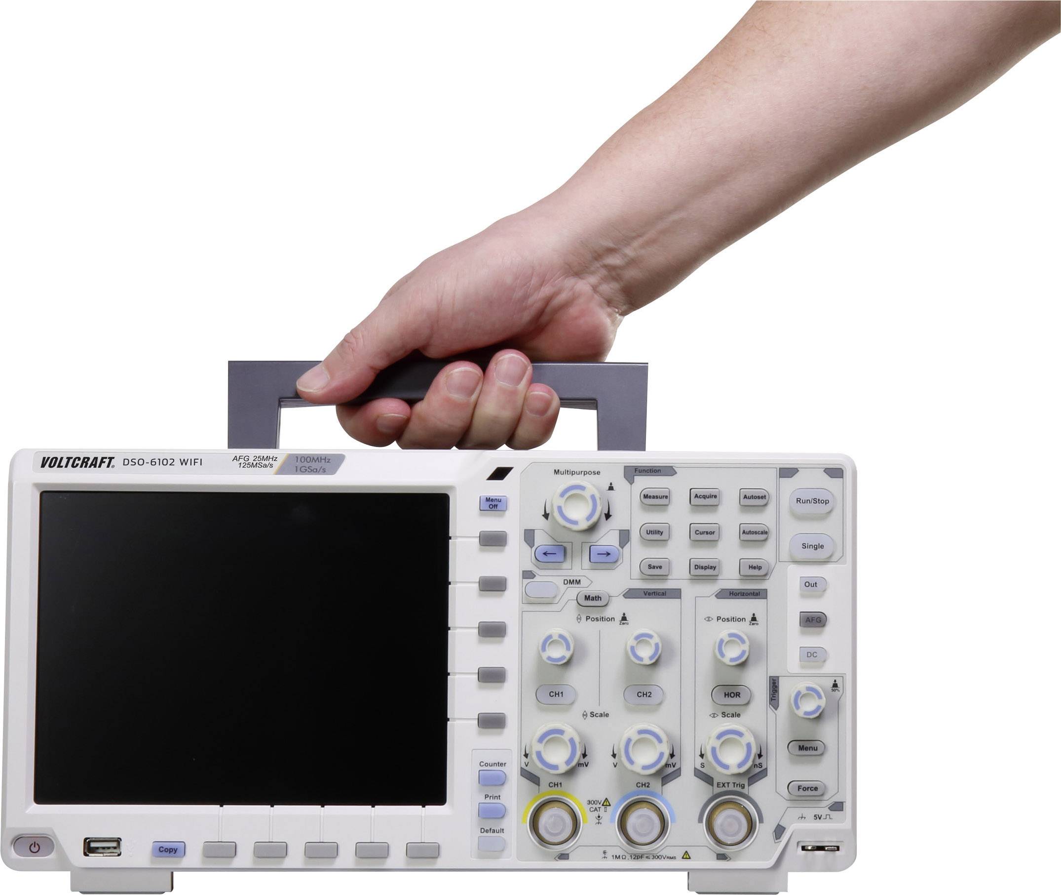 Jedna ruka drží přenosný osciloskop, model Voltcraft DSO-6102 WIFI, s displejem a několika otočnými ovládacími knoflíky.
