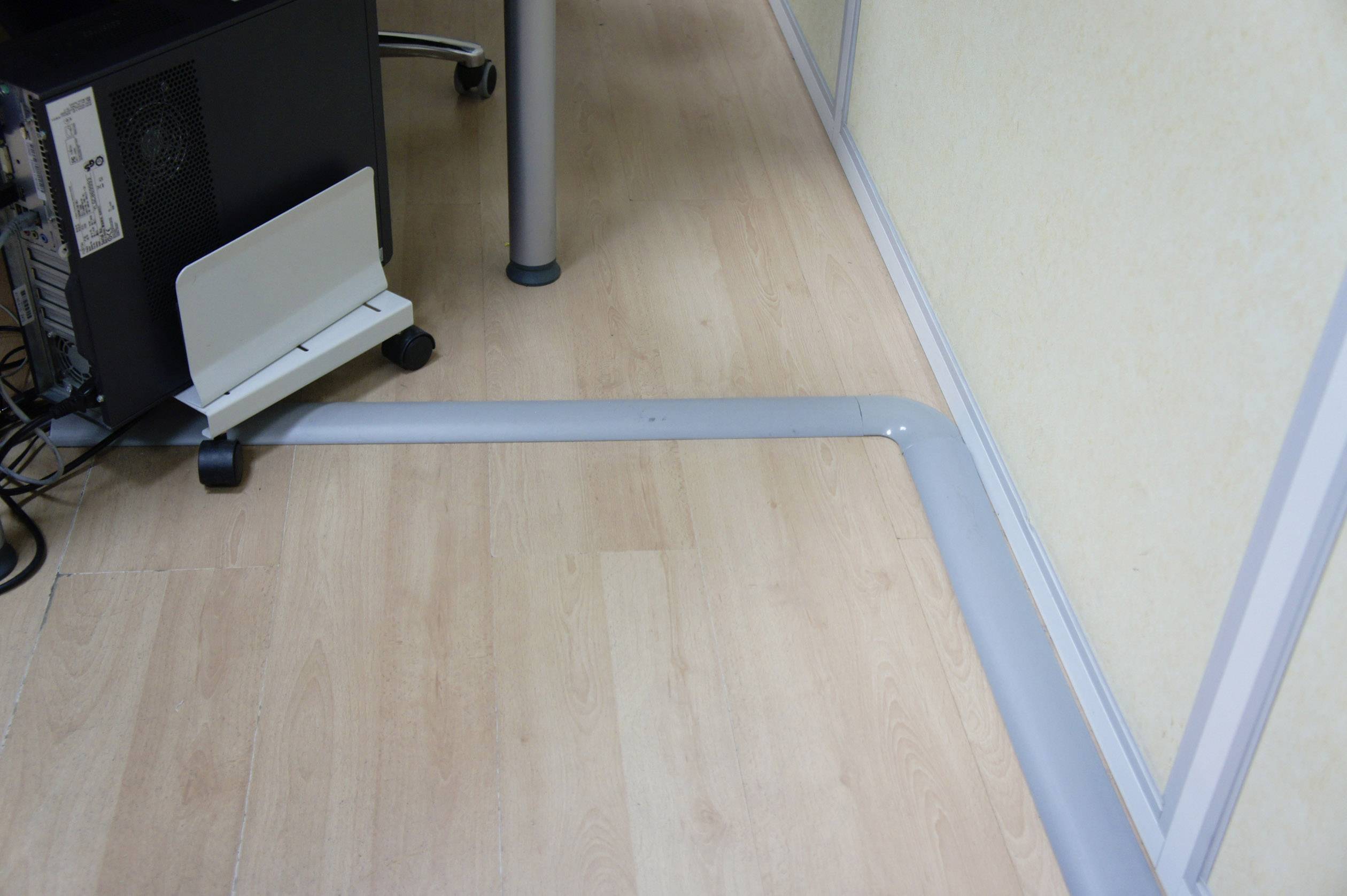 Kabelový kanál vede podél stěny na dřevěné podlaze, aby bezpečně vedl kabely a předcházel riziku zakopnutí.