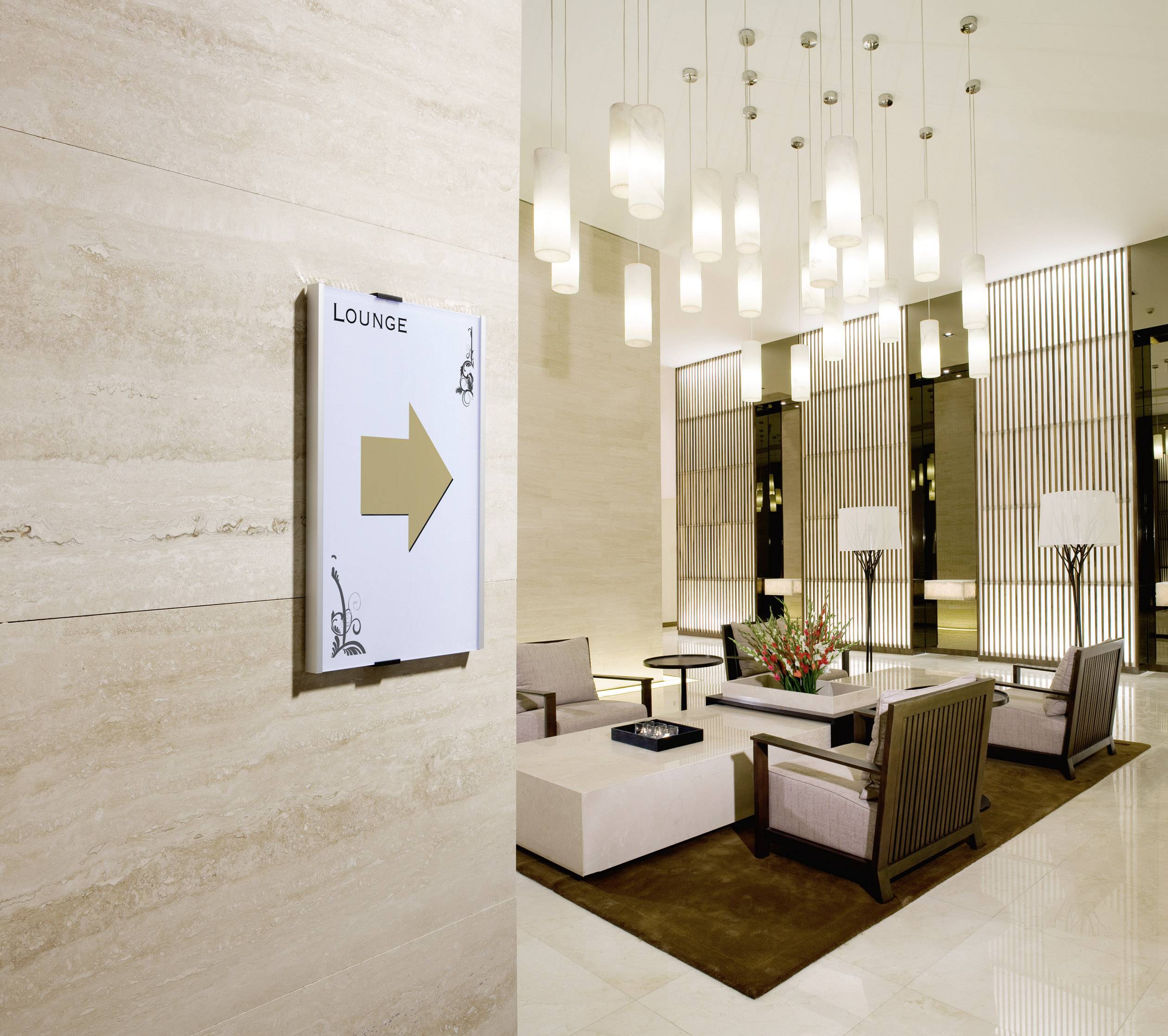 Elegantní hotelová hala s moderním nábytkem, nenápadnými osvětlovacími prvky a navigační tabulí s nápisem "Lounge" a šipkou.