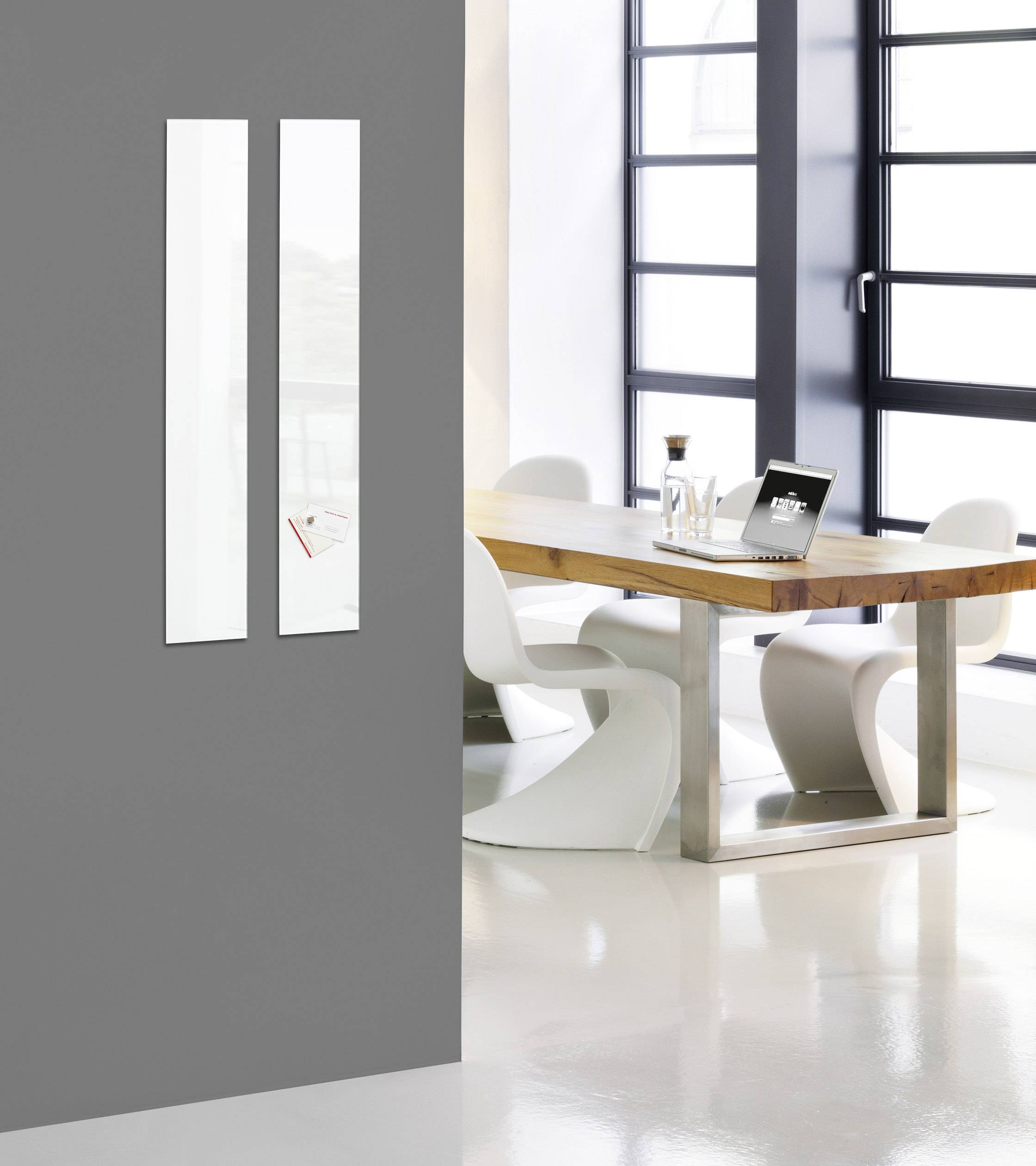 Moderní zasedací místnost, dřevěný stůl s bílými židlemi. Velká okna zajišťují dostatek denního světla. V pozadí minimalistický design.