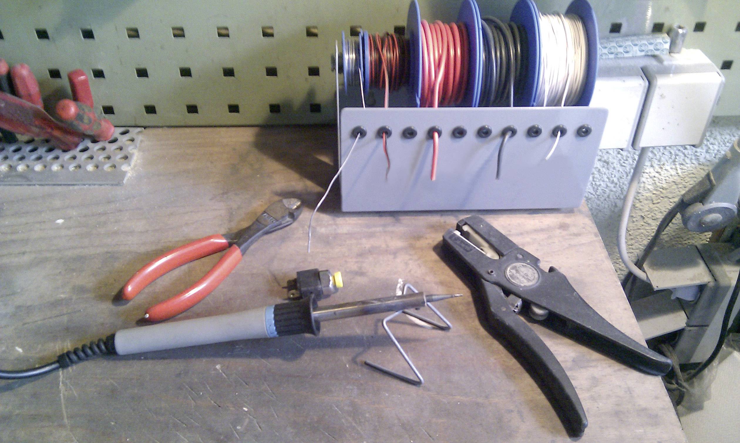 Pracovní stůl s pájecí stanicí, kleštěmi, odizolovacím nástrojem a cívkami drátů. Připraveno pro elektronické práce.