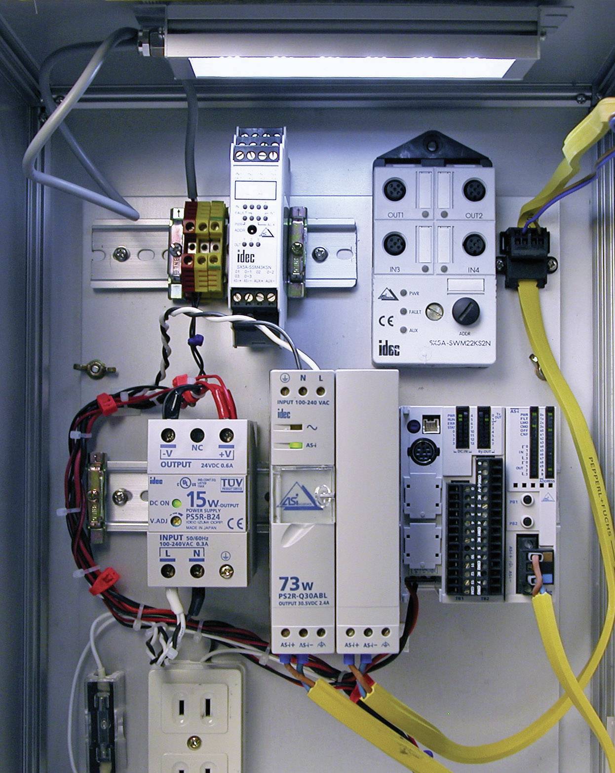 Otevřená rozvodná skříň s různými elektronickými komponenty a vodiči, včetně napájecího zdroje, relé a zásuvky.