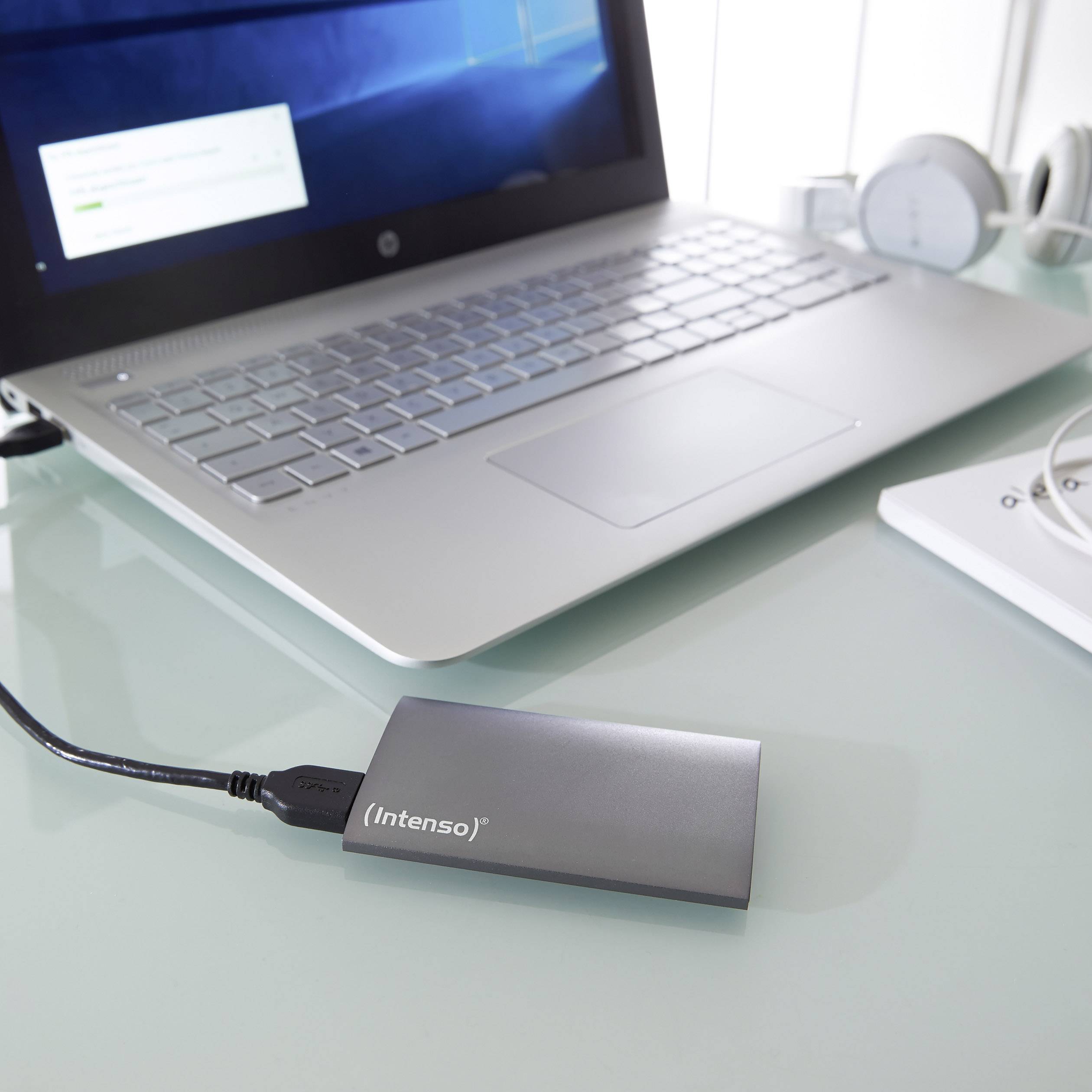 Externí pevný disk 'Intenso' připojený k notebooku na pracovním stole, symbolizuje přenos dat nebo zálohování.