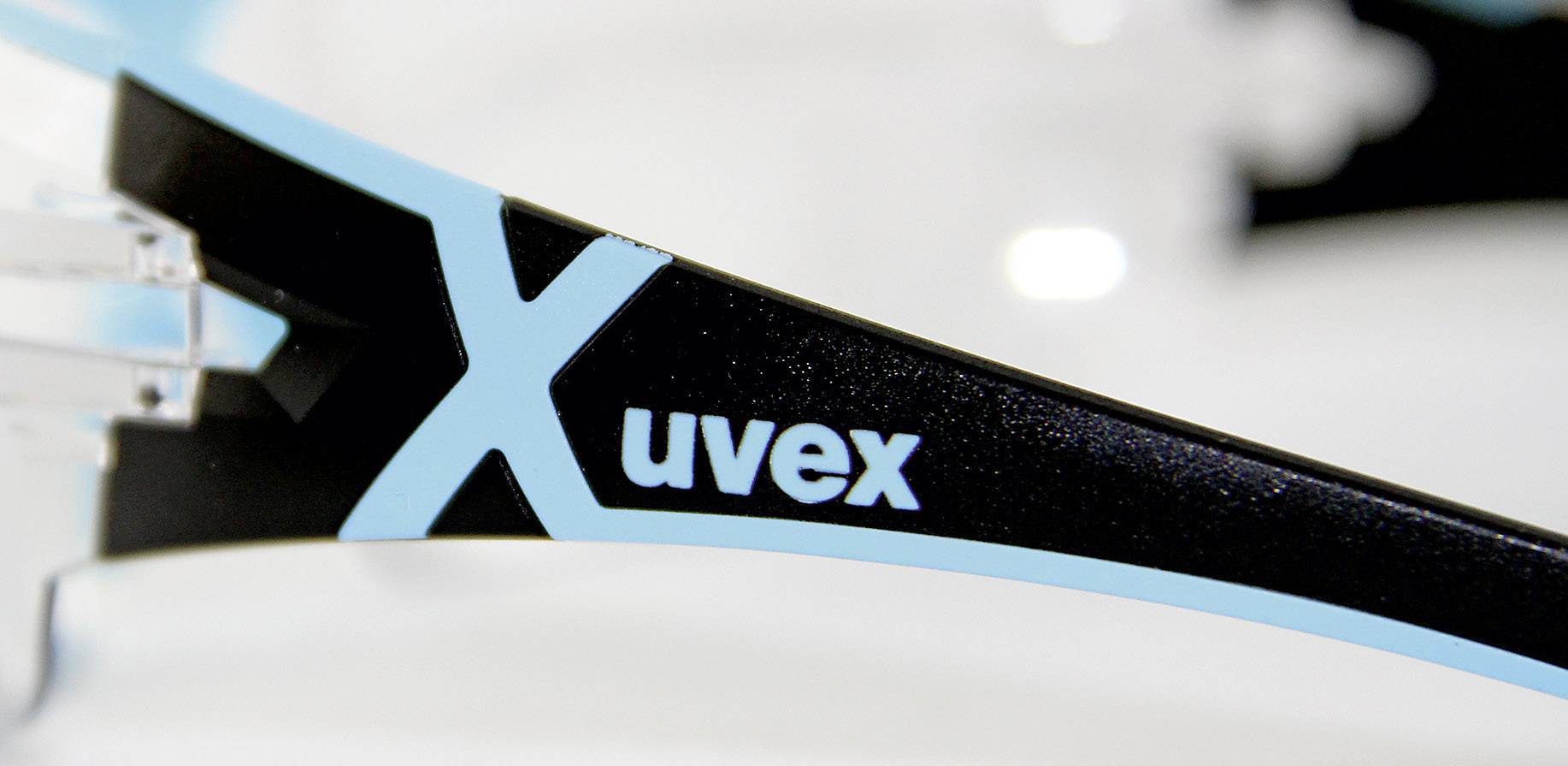 Detailní záběr stranice brýlí s názvem značky 'uvex' a velkým modrým 'X'. Stranice má černé a modré barevné provedení.