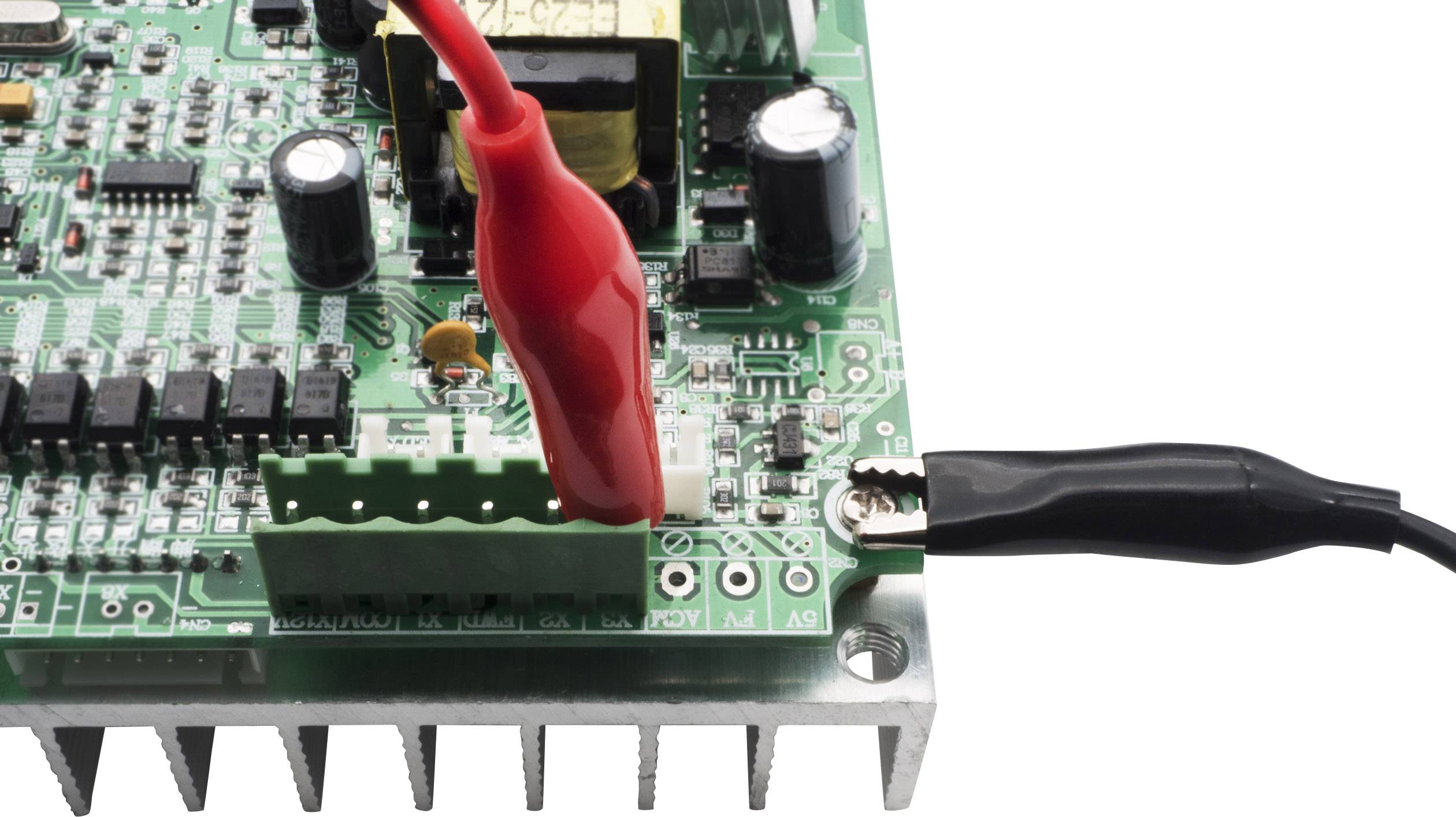 Zelená deska plošných spojů s elektronickými komponenty. Dva krokosvorky jsou připojeny k desce a vedou elektrický proud.