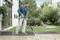 Muž čistí terasu vysokotlakým čističem. V pozadí jsou vidět rostliny a dům.